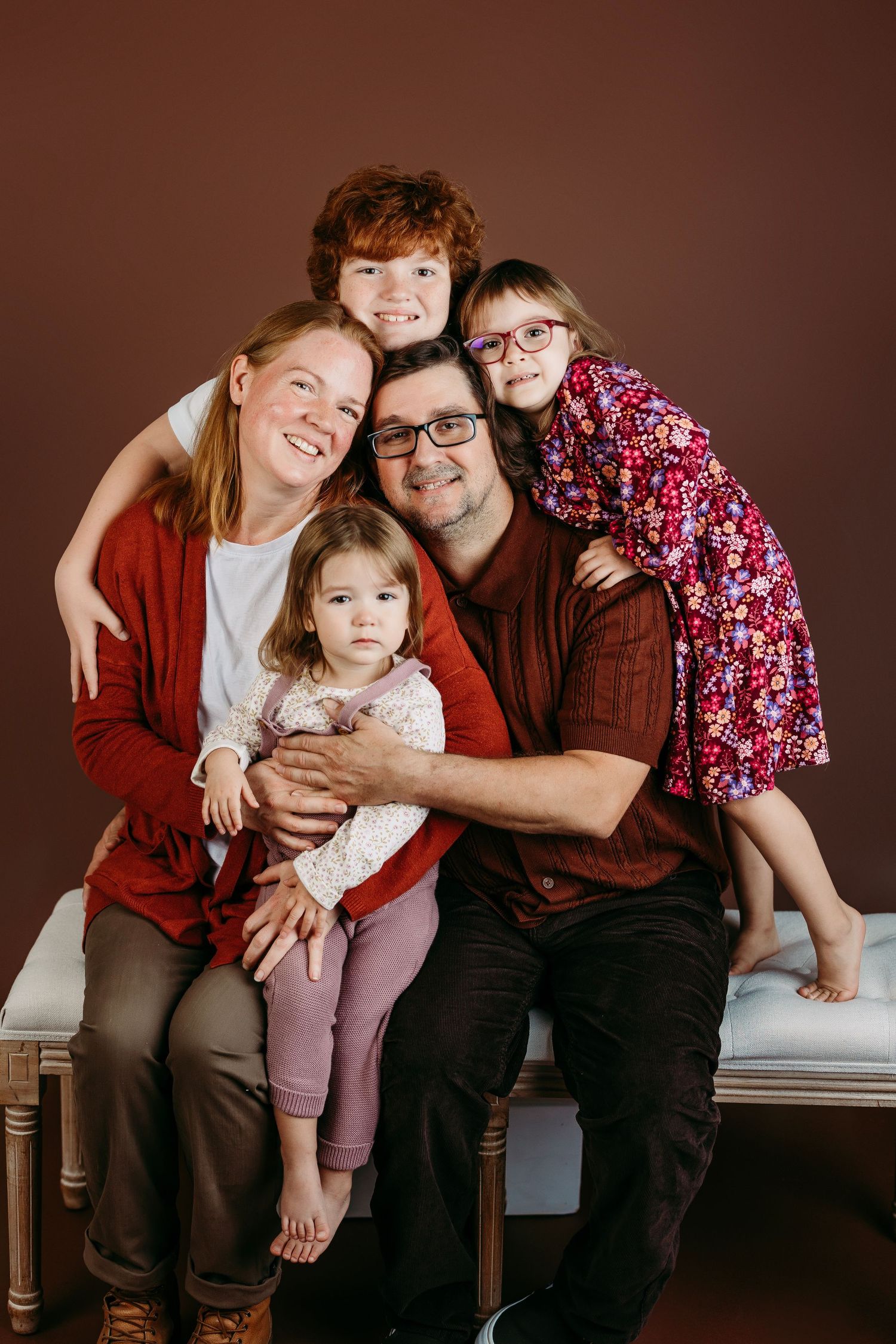 Family portrait series showing candid moments of parents and children sitting together on a wooden bench.