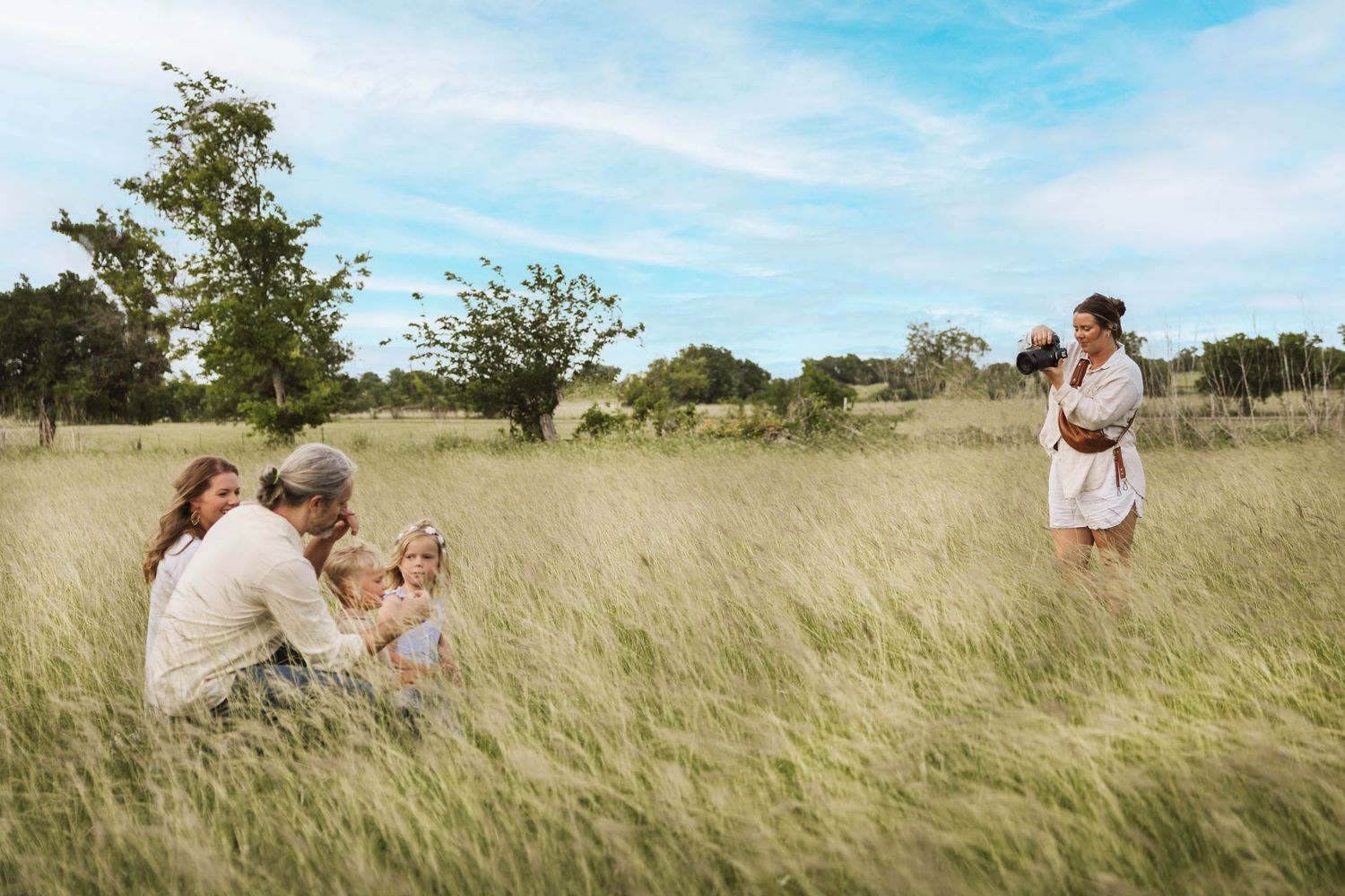 Family enjoying a candid moment together in a sun-drenched field of tall grass during golden hour.