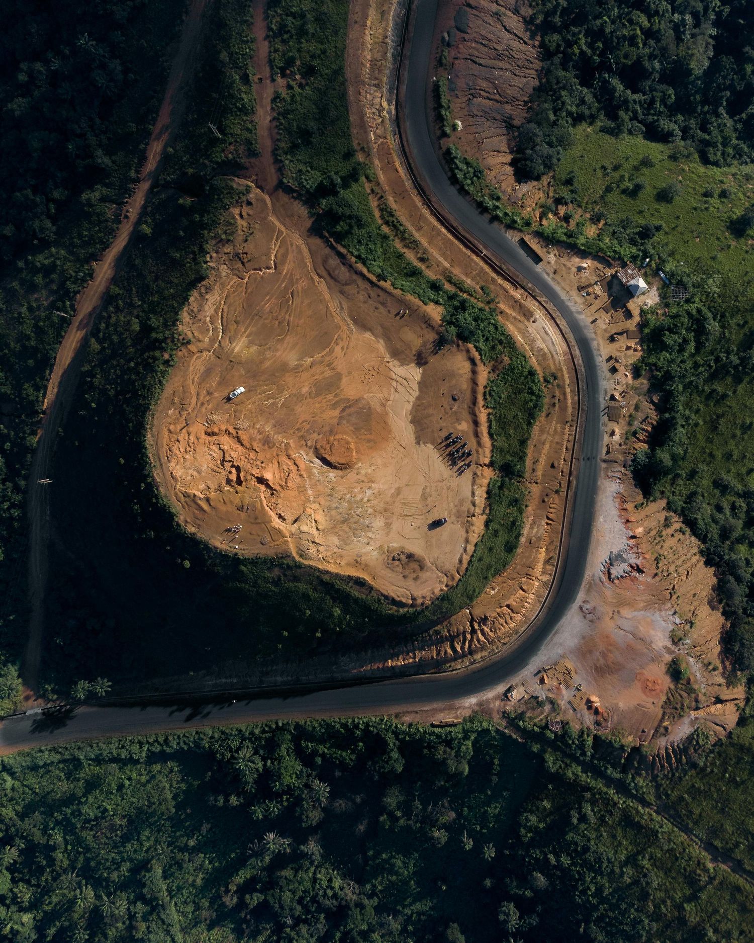 Aerial view of a curved road cutting through cleared earthen terrain surrounded by forest.