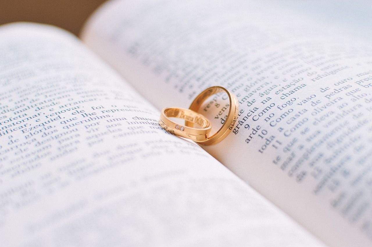 Gold wedding bands rest on the pages of an open book creating a heart shadow in soft natural light.