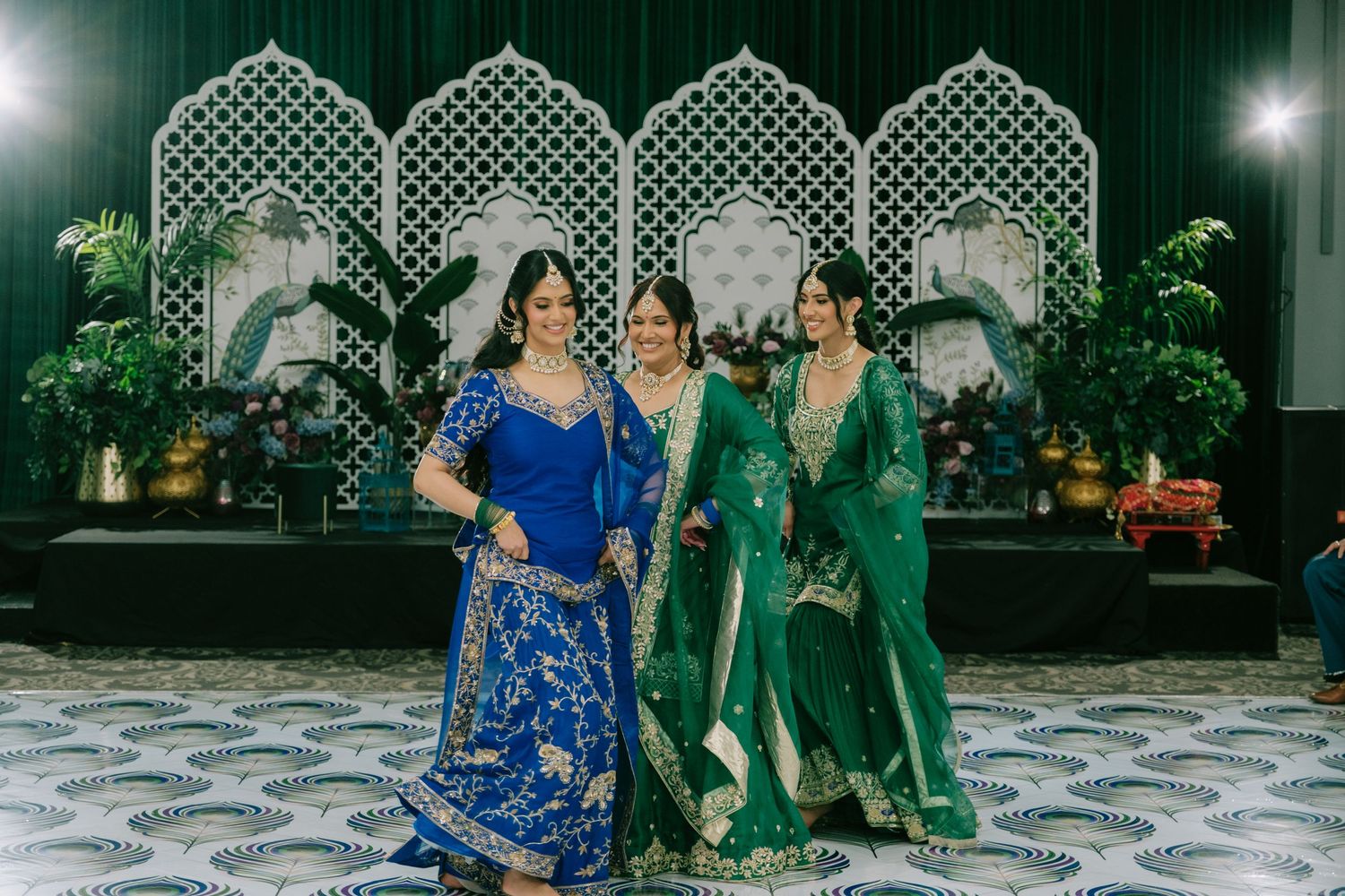 South Asian wedding celebration with traditional formal attire in front of an ornate white latticed backdrop at night.