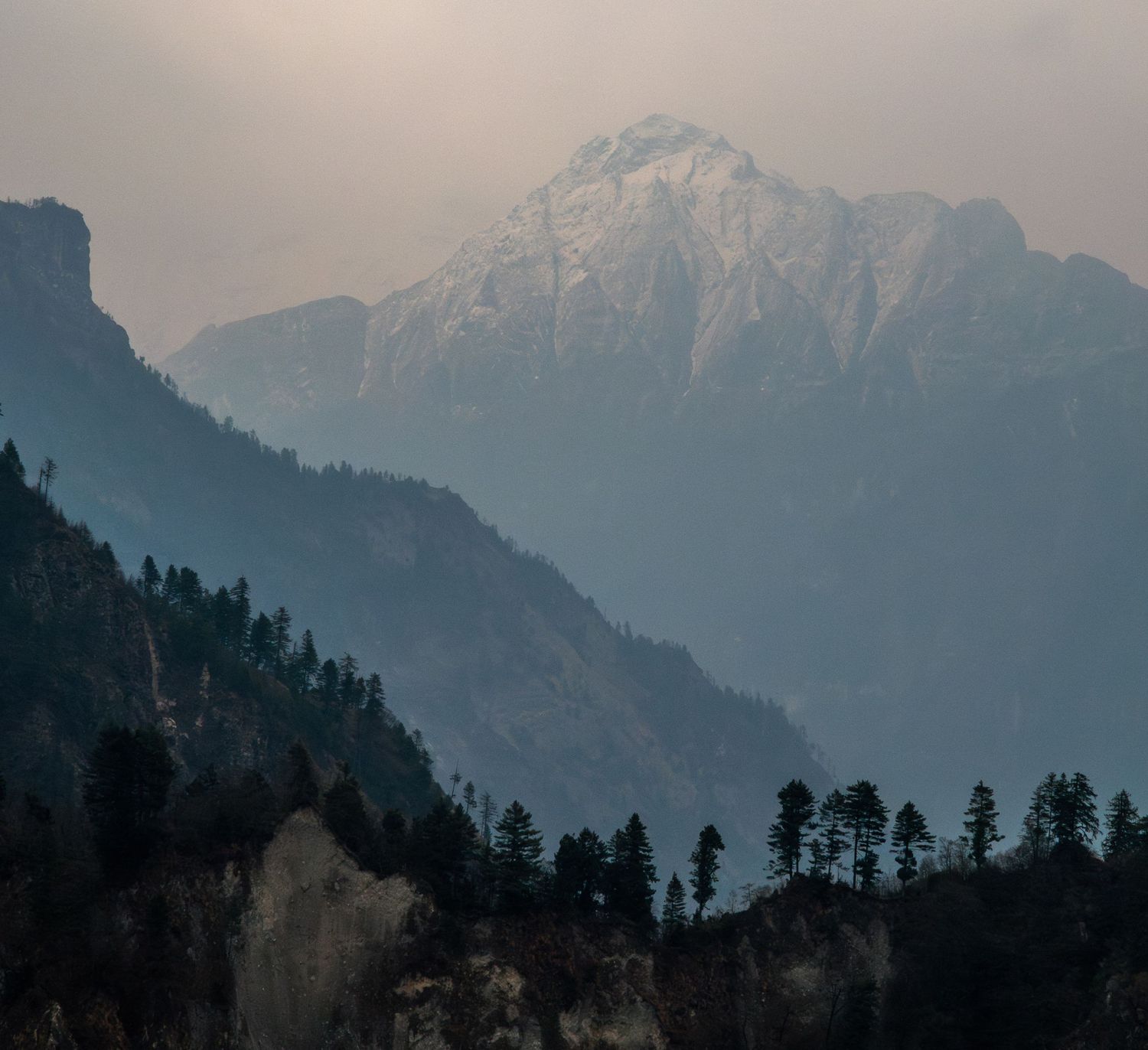 Misty mountain silhouettes with snow-capped peaks in hazy evening light.