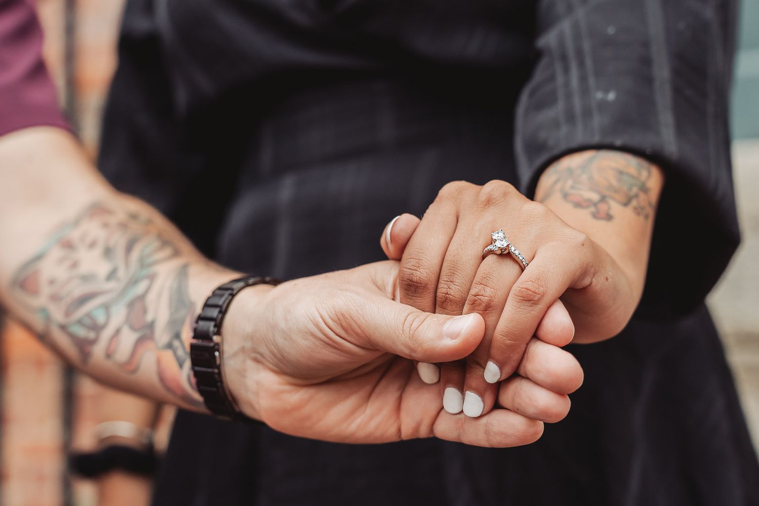 Detailed shot of engagement ring on tattooed hand with watch detail.
