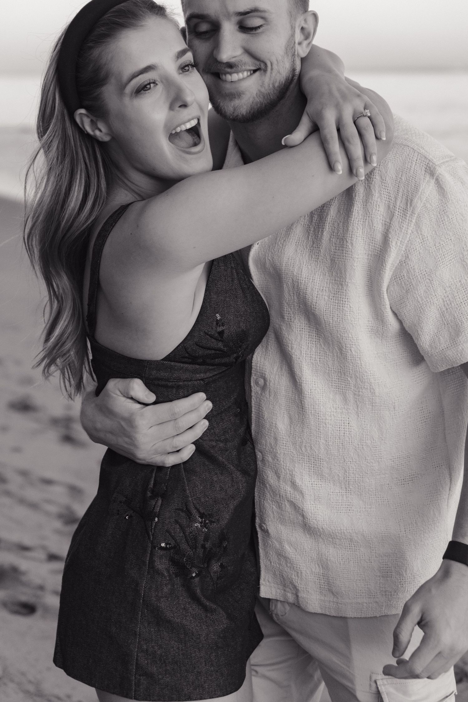 A joyful couple embraces and laughs together on the beach in black and white photography.