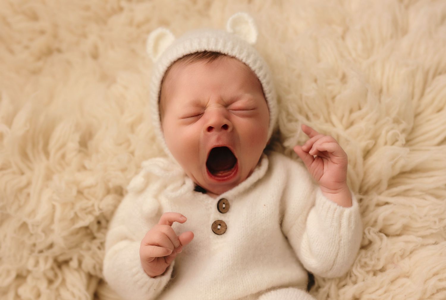 Charlottesville newborn photographer, sleepy baby boy dressed in white knit body suit and hat yawns during a studio session.
