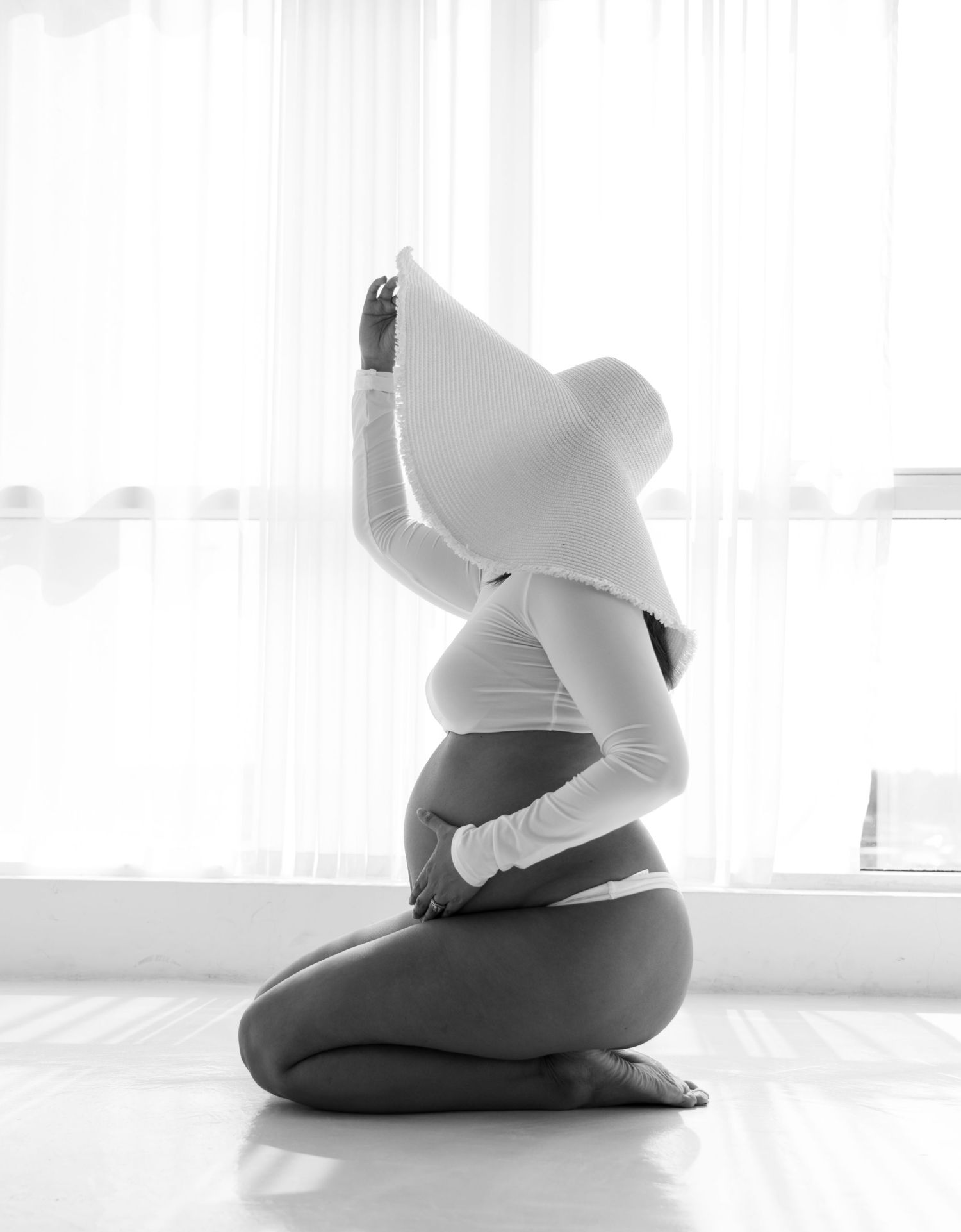 A person in black and white workout attire practices a kneeling yoga pose against a bright window backdrop.