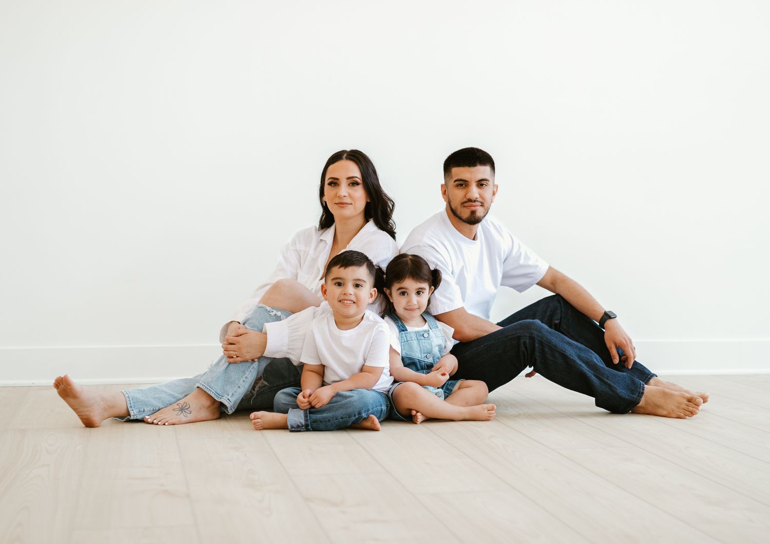 A family of four sits together against a white backdrop in coordinated casual outfits.