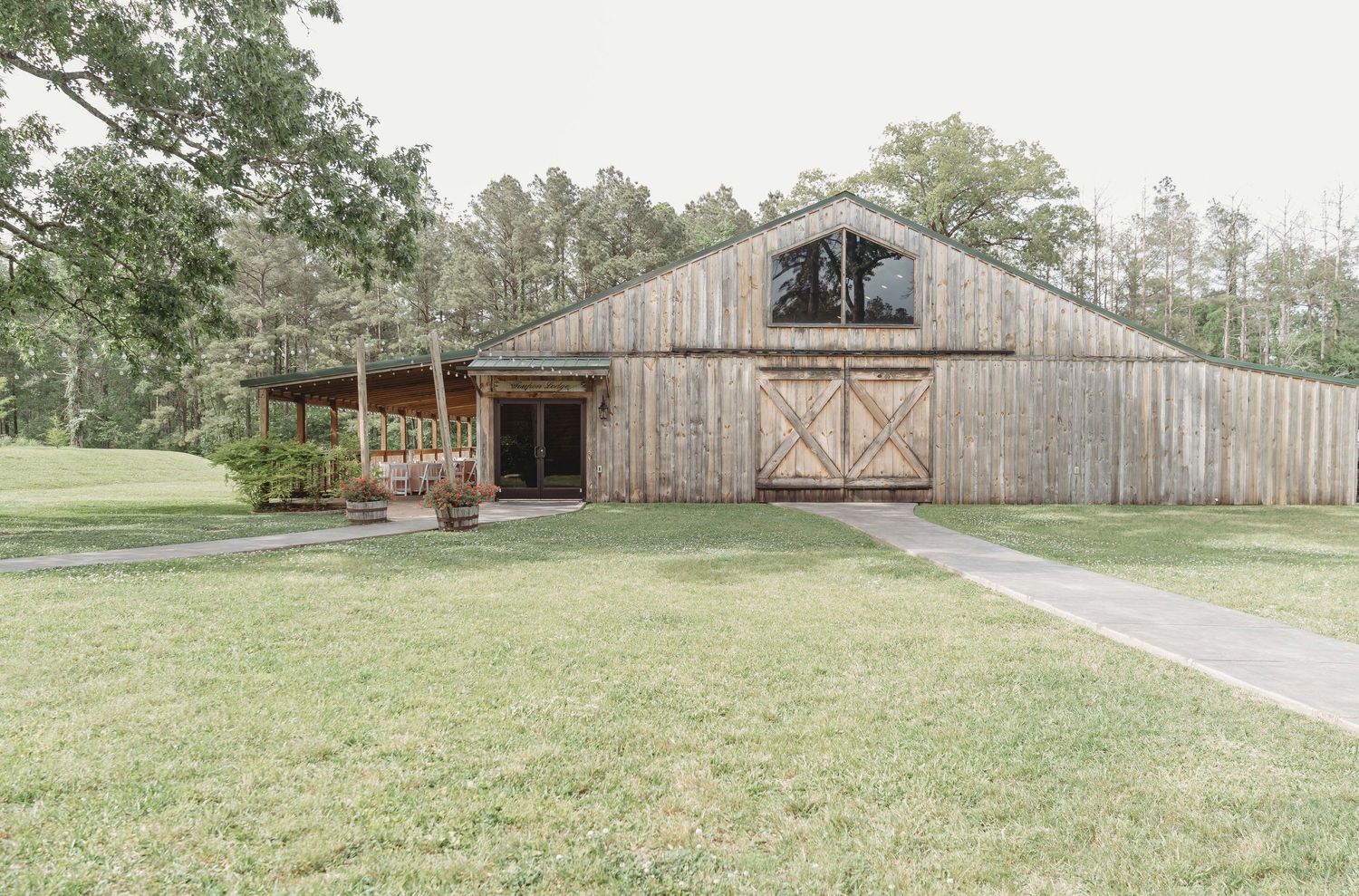 A rustic wooden barn with porch on landscaped lawn features weathered siding and cross-shaped barn doors.