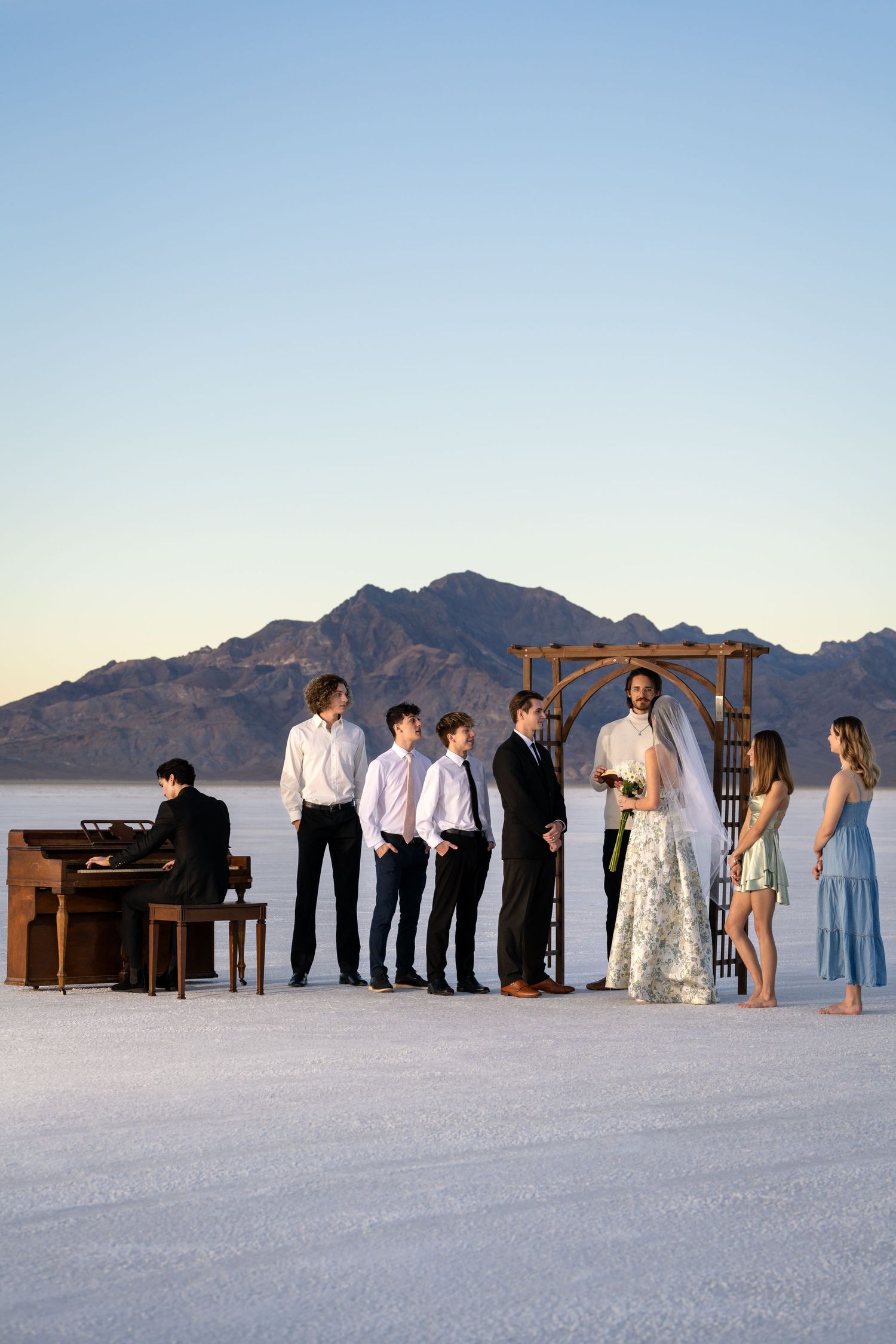 A wedding ceremony setup on salt flats with mountains and piano at sunset.