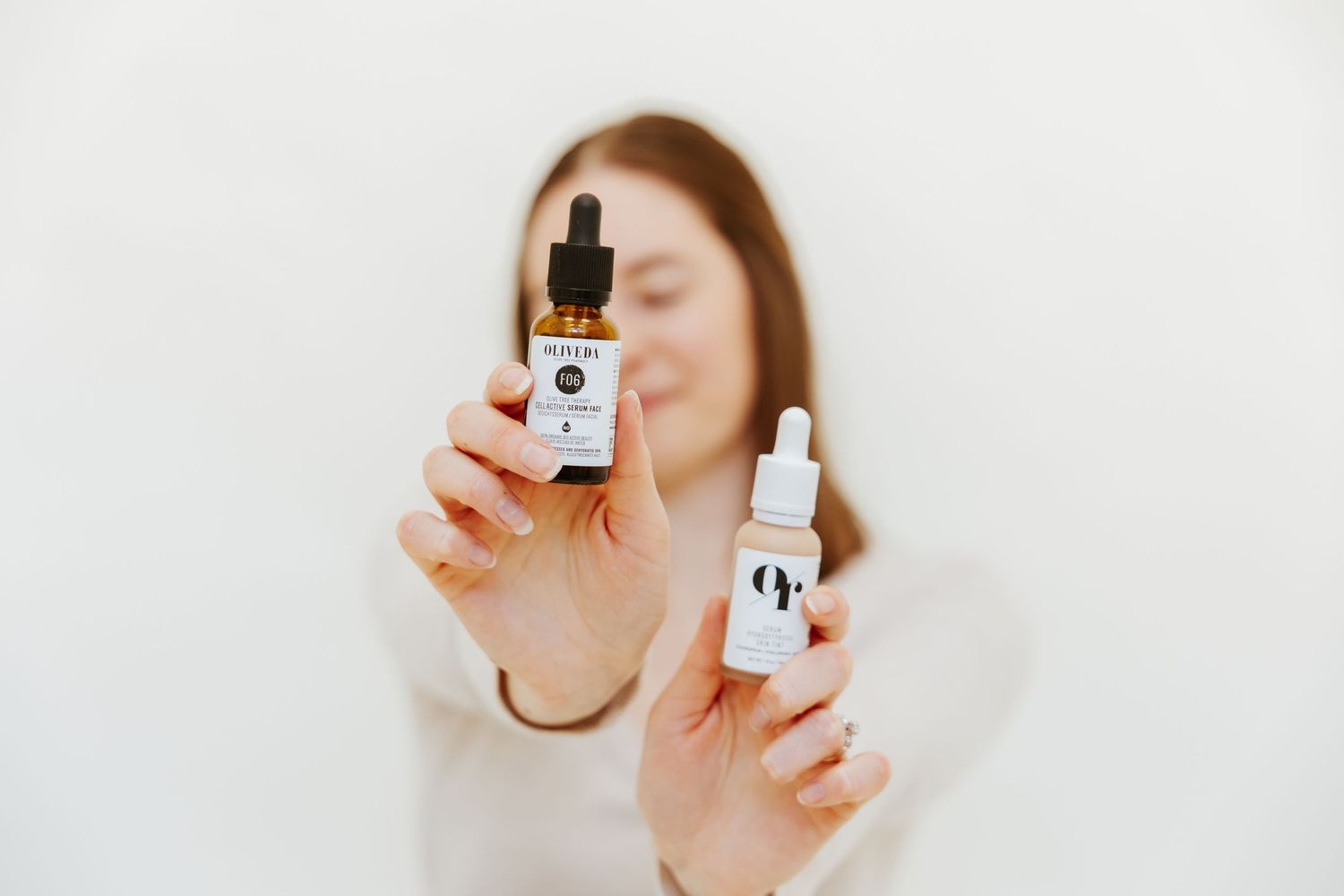 Hands holding up CBD oil dropper bottles against white background.