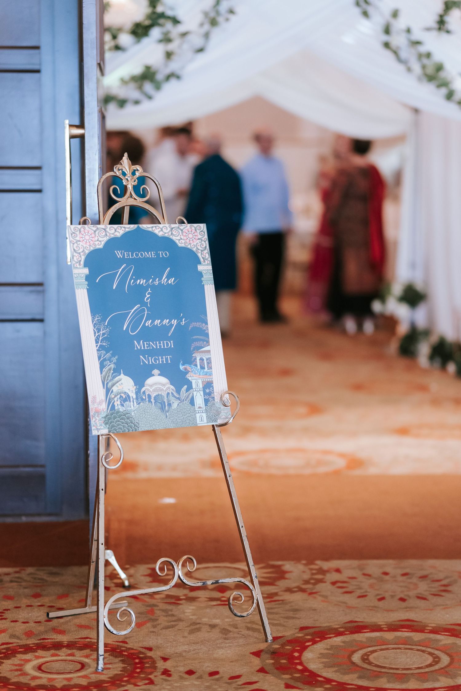 Elegant wedding welcome sign with blue and white design on ornate metal easel stand.