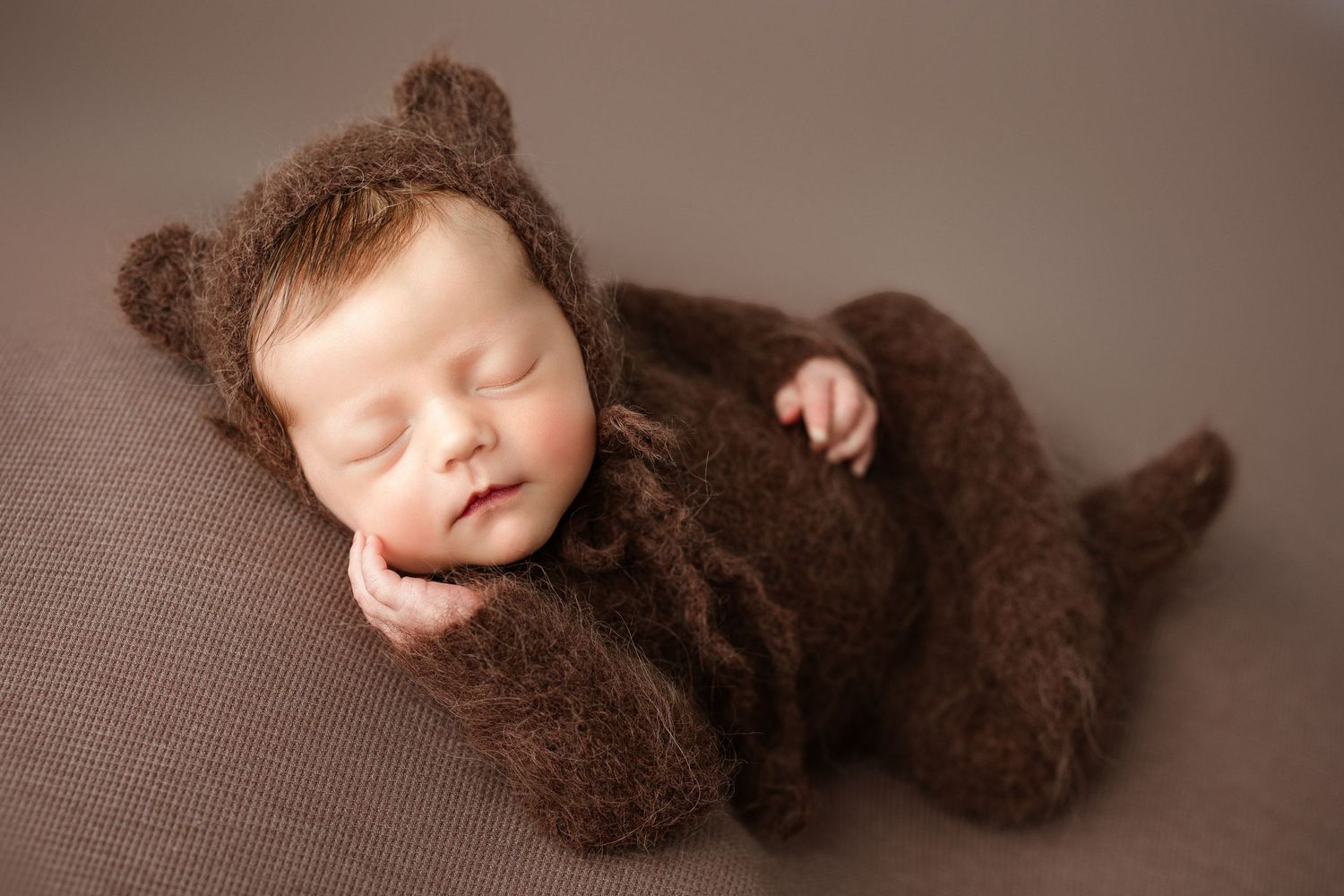 A sleeping newborn wearing a brown knit outfit lies peacefully in a studio photography setting. Middle TN Newborn Photographer.
