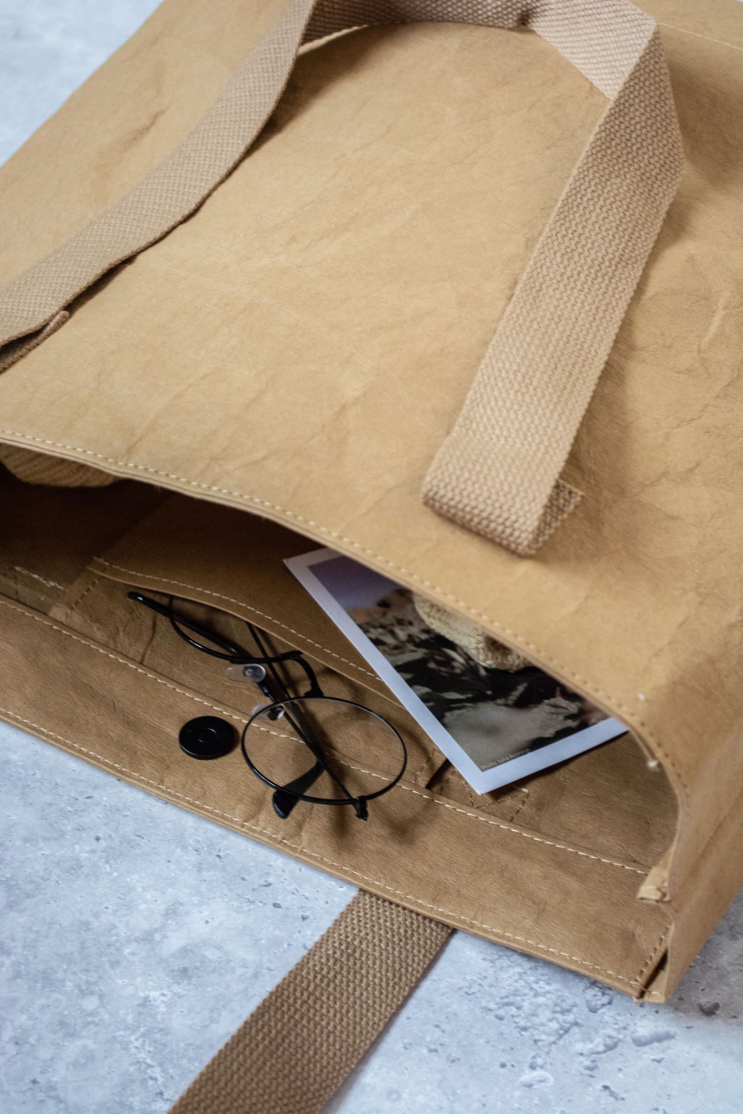 Tan canvas bag with straps laying flat on a light surface, showing contents peeking out.