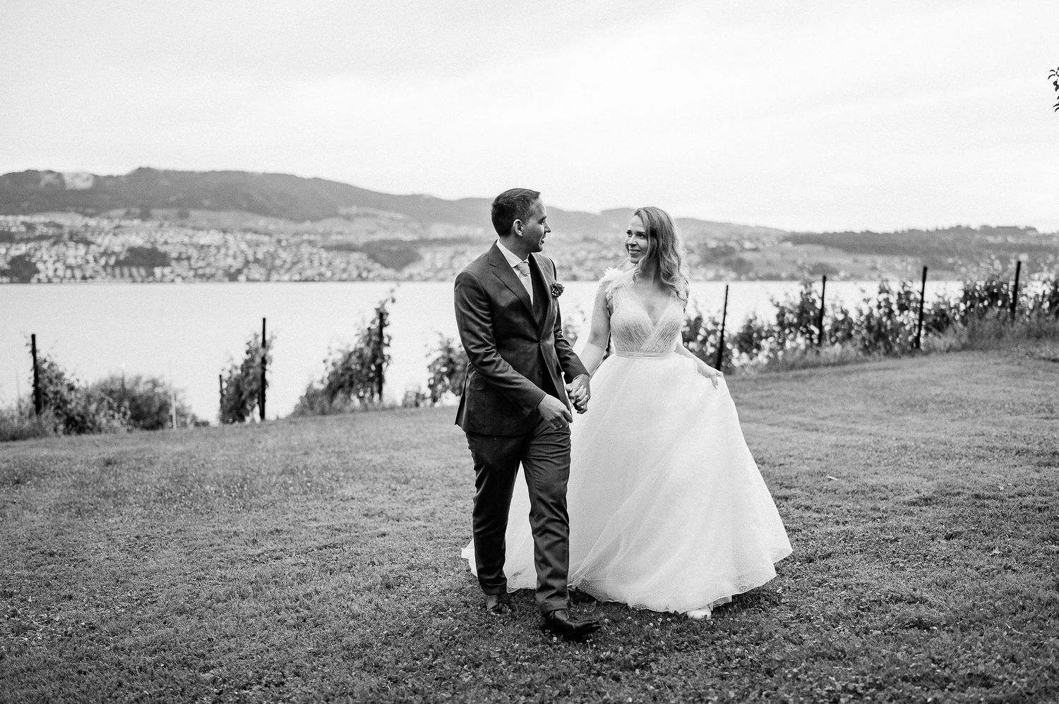 A scenic black and white wedding photo overlooking rolling hills and a lake on a beautiful countryside landscape.