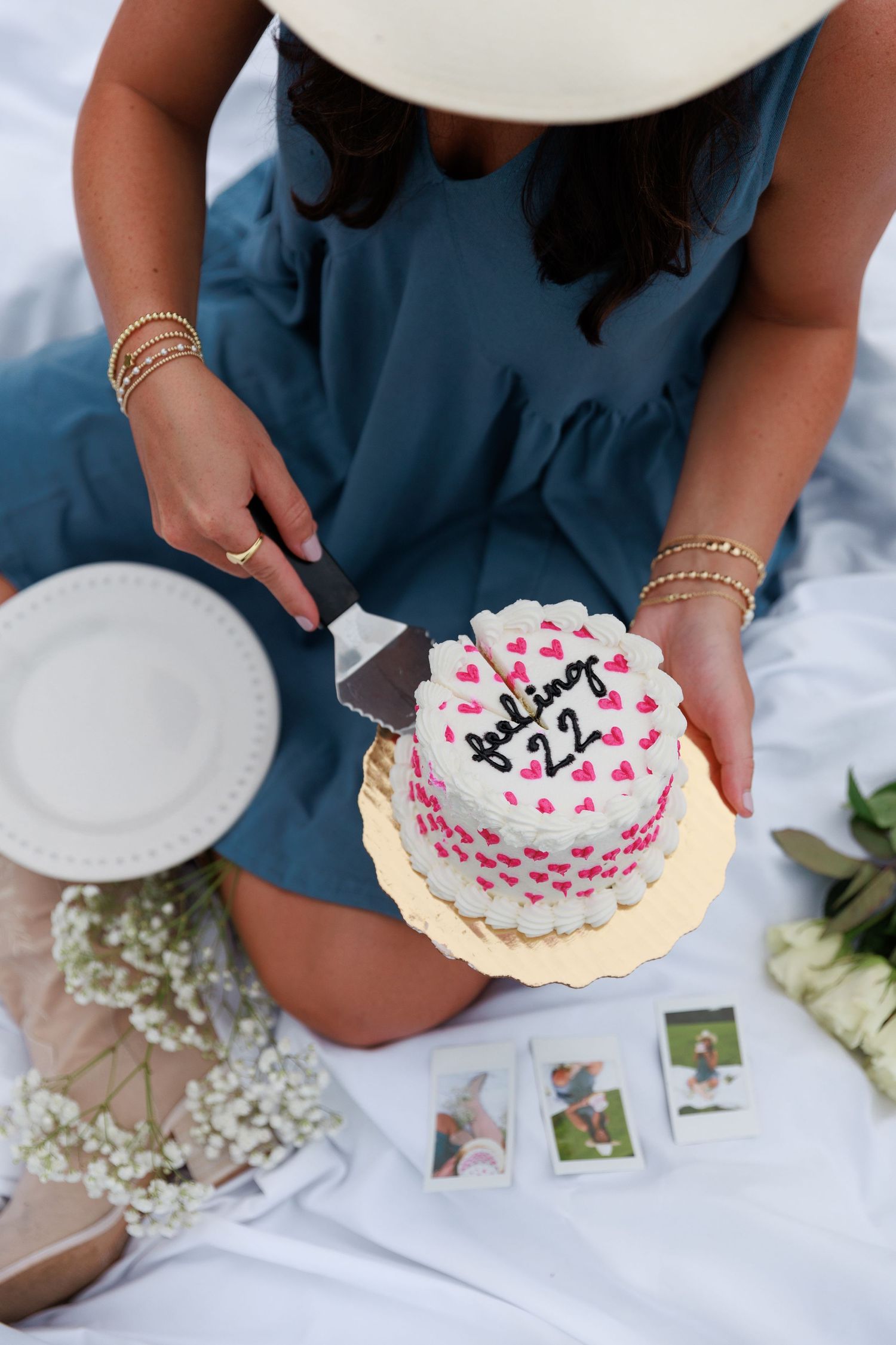 Overhead view of birthday cake with pink hearts and decorative flowers on white blanket.
