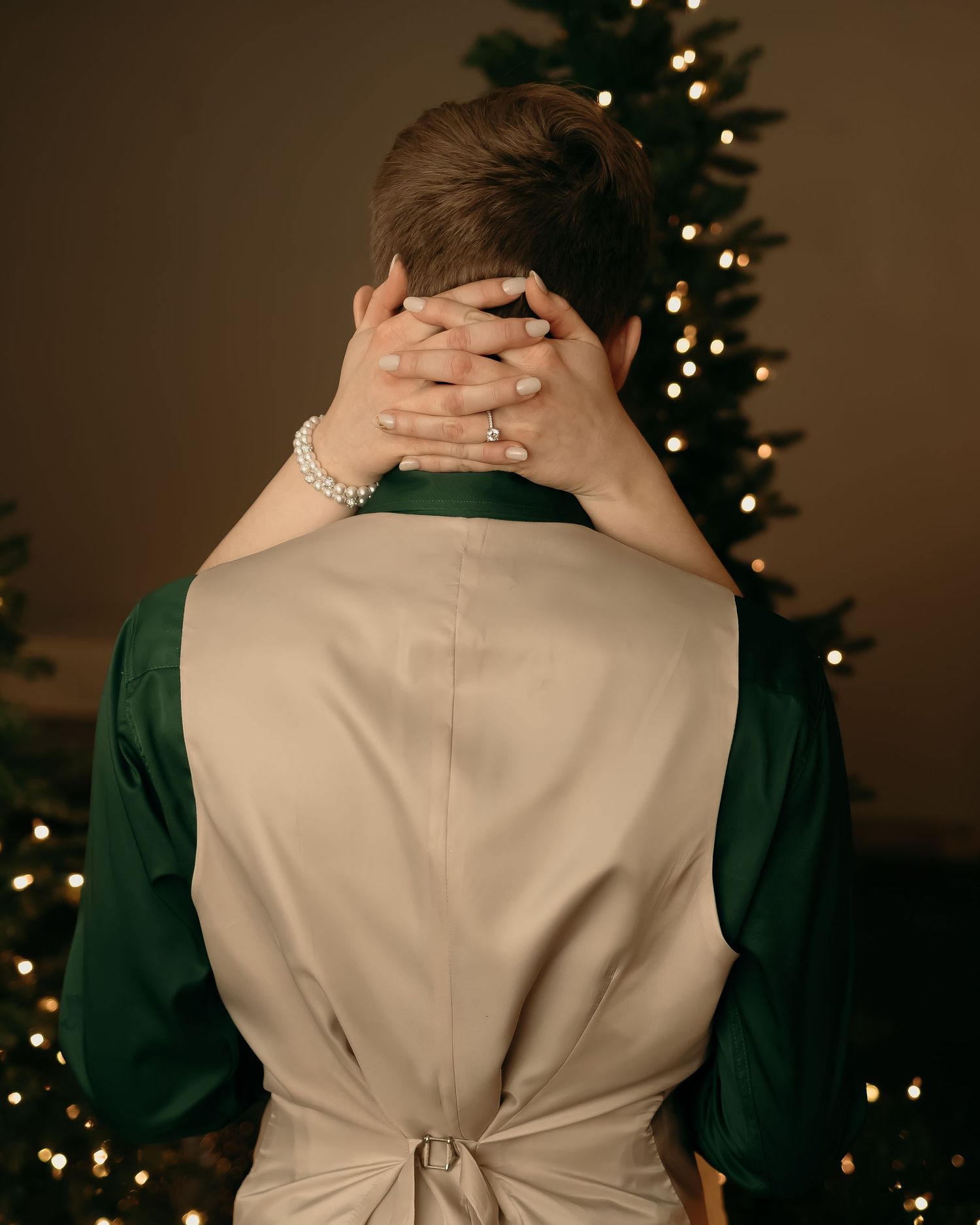 Person wearing a beige and green outfit faces away from camera in front of illuminated Christmas tree at home.