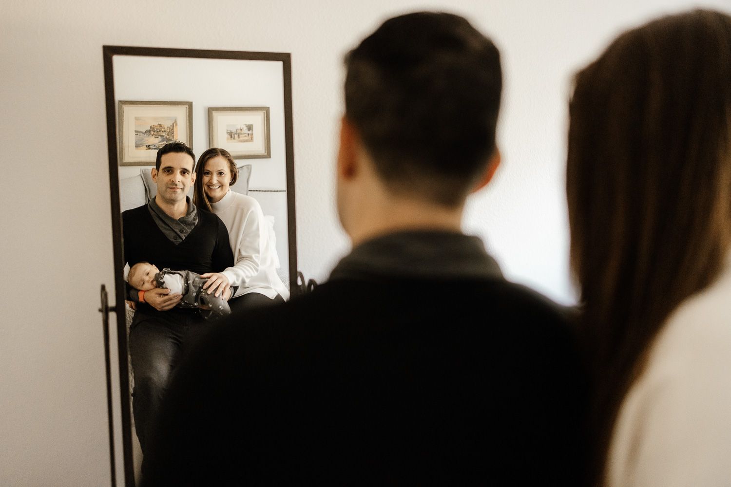 Parents hold their new baby while looking in a mirror at newborn photo session with Cindy Tucey Photography in San Jose