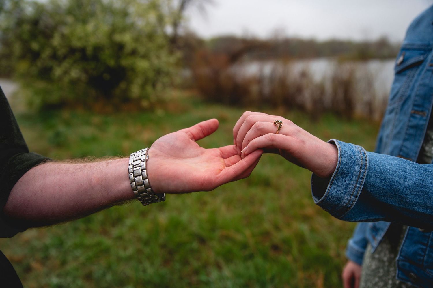 Two hands reaching toward each other with one wearing a silver bracelet against a blurred natural background.