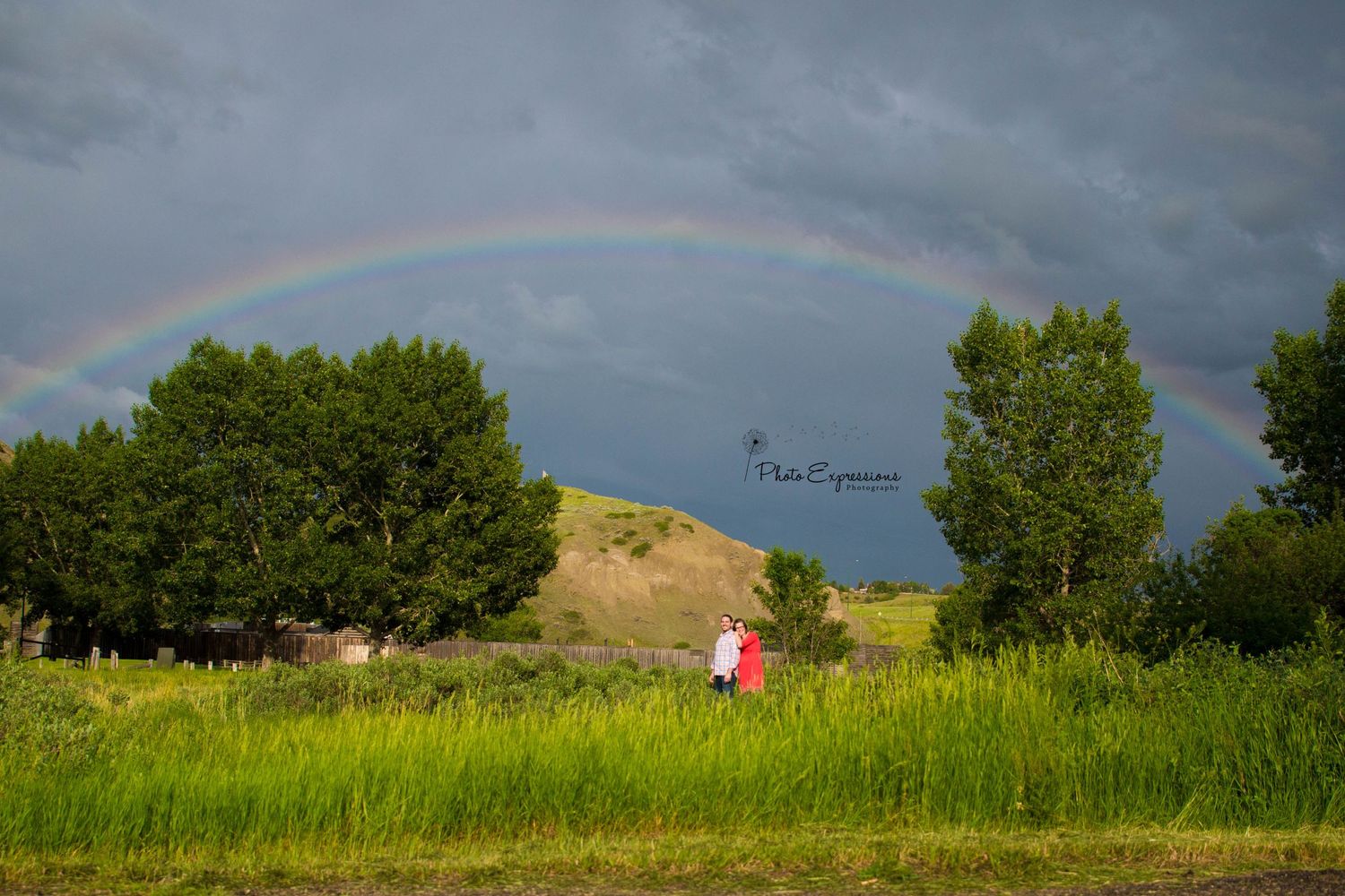 Double rainbow arches over green landscape with trees and hills.