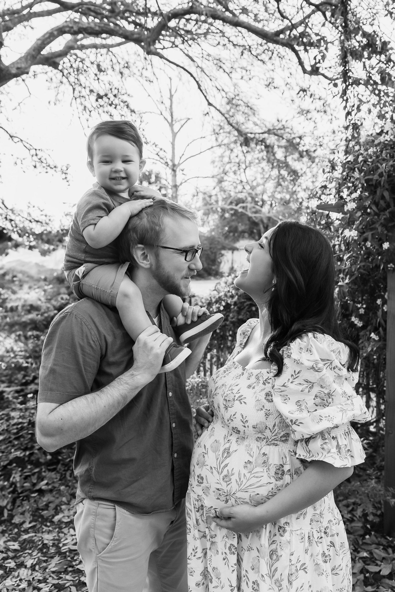 A joyful black and white family photo captured outdoors under tree branches in natural lighting.
