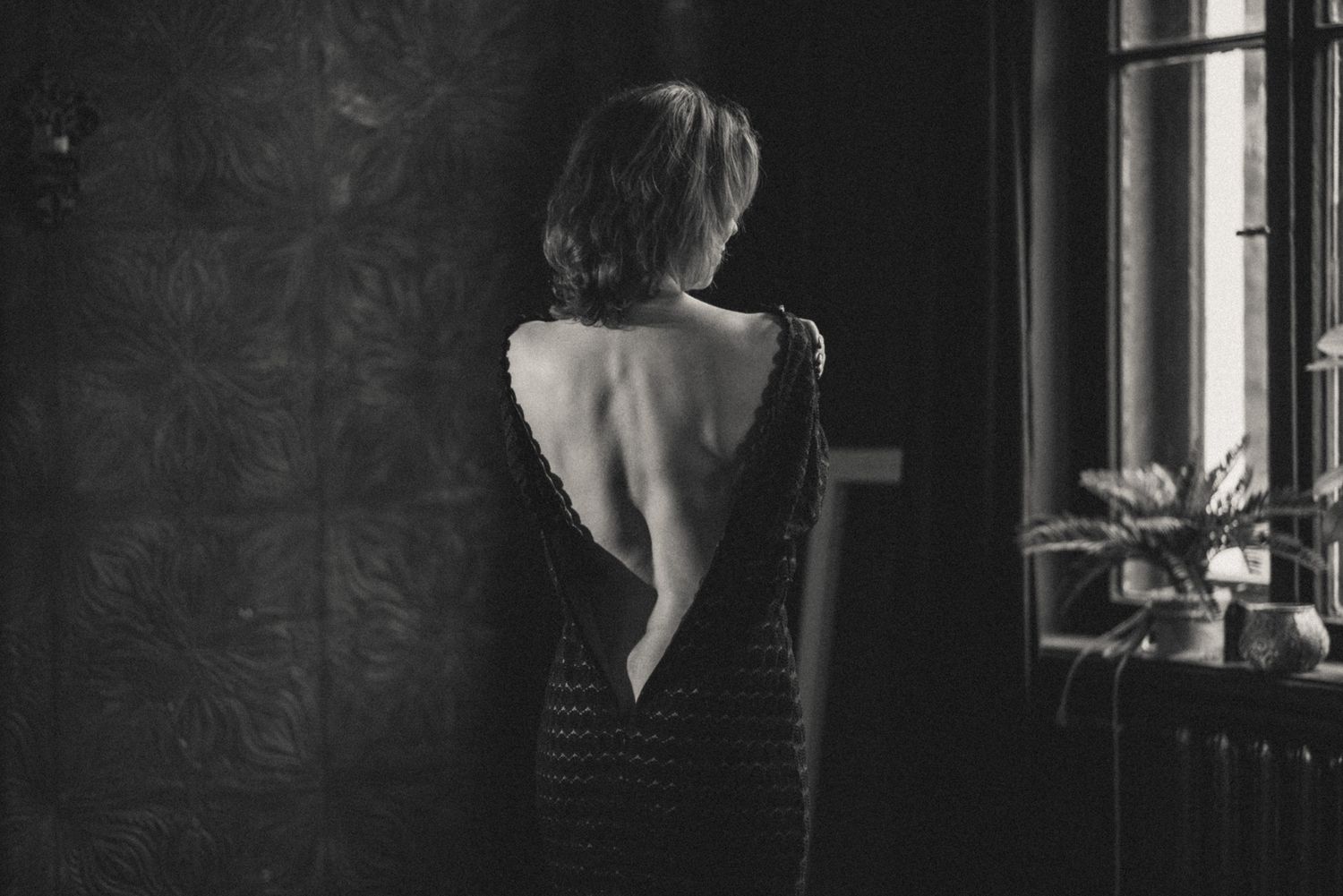 Black-and-white boudoir photo: a woman photographed from the back, dress zipper undone, exposing her bare back.