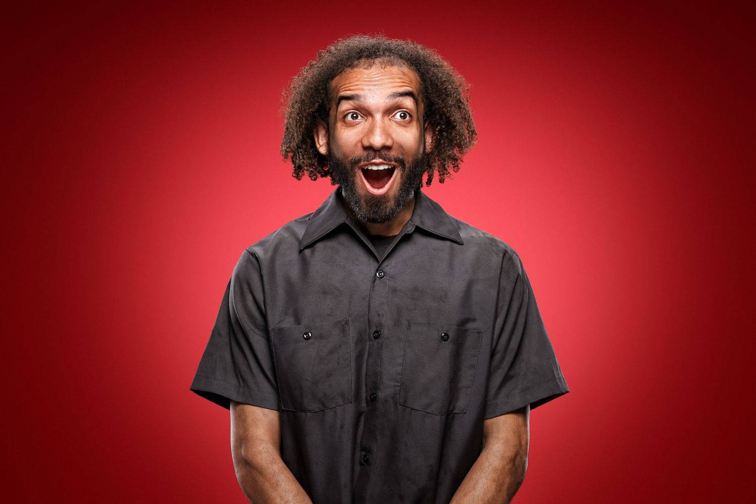 Portrait of a person with curly hair expressing excitement against a red background.