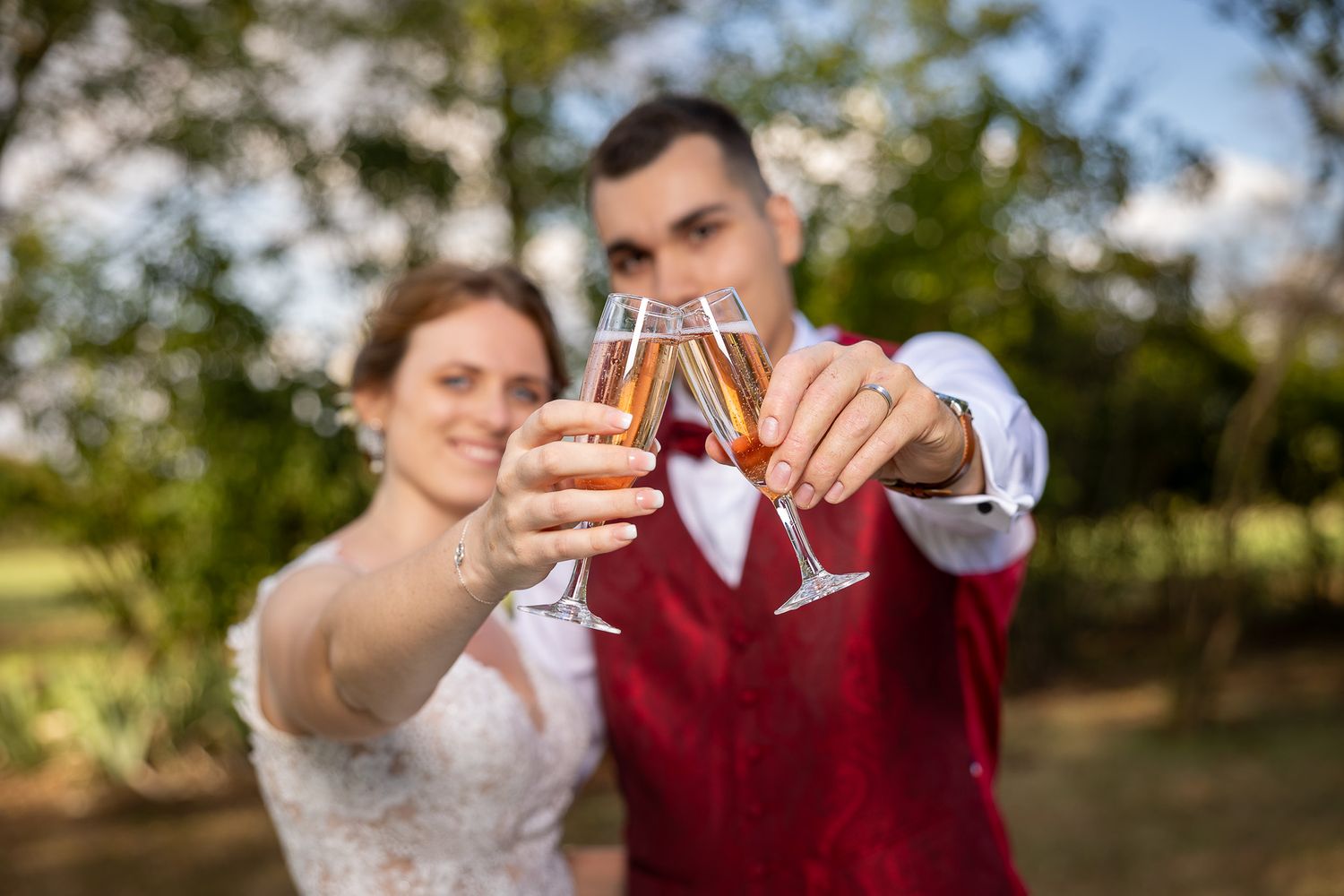 Wedding couple toasting with wine glasses in an outdoor garden setting with soft bokeh background.