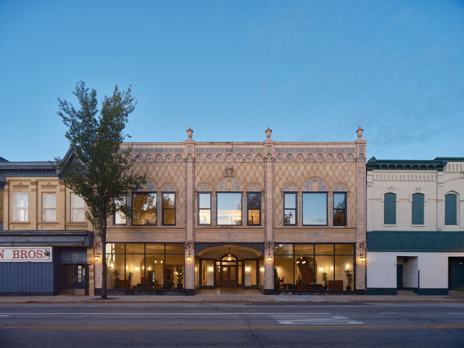 Illuminated historic brick building facade with decorative trim and large windows at dusk.