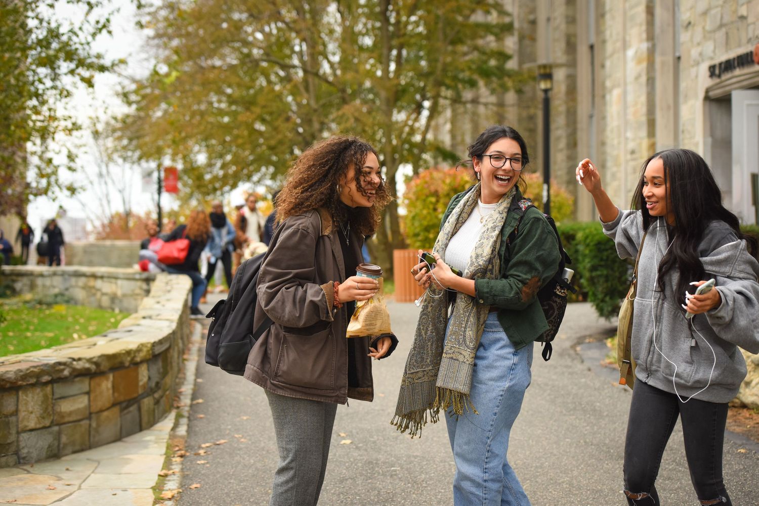 Students walking and laughing together on a college campus pathway during autumn.