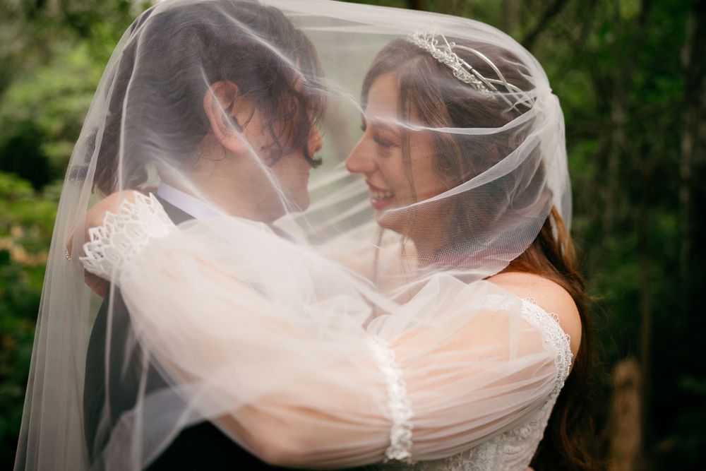 A romantic wedding moment captured under a flowing veil in an outdoor setting.