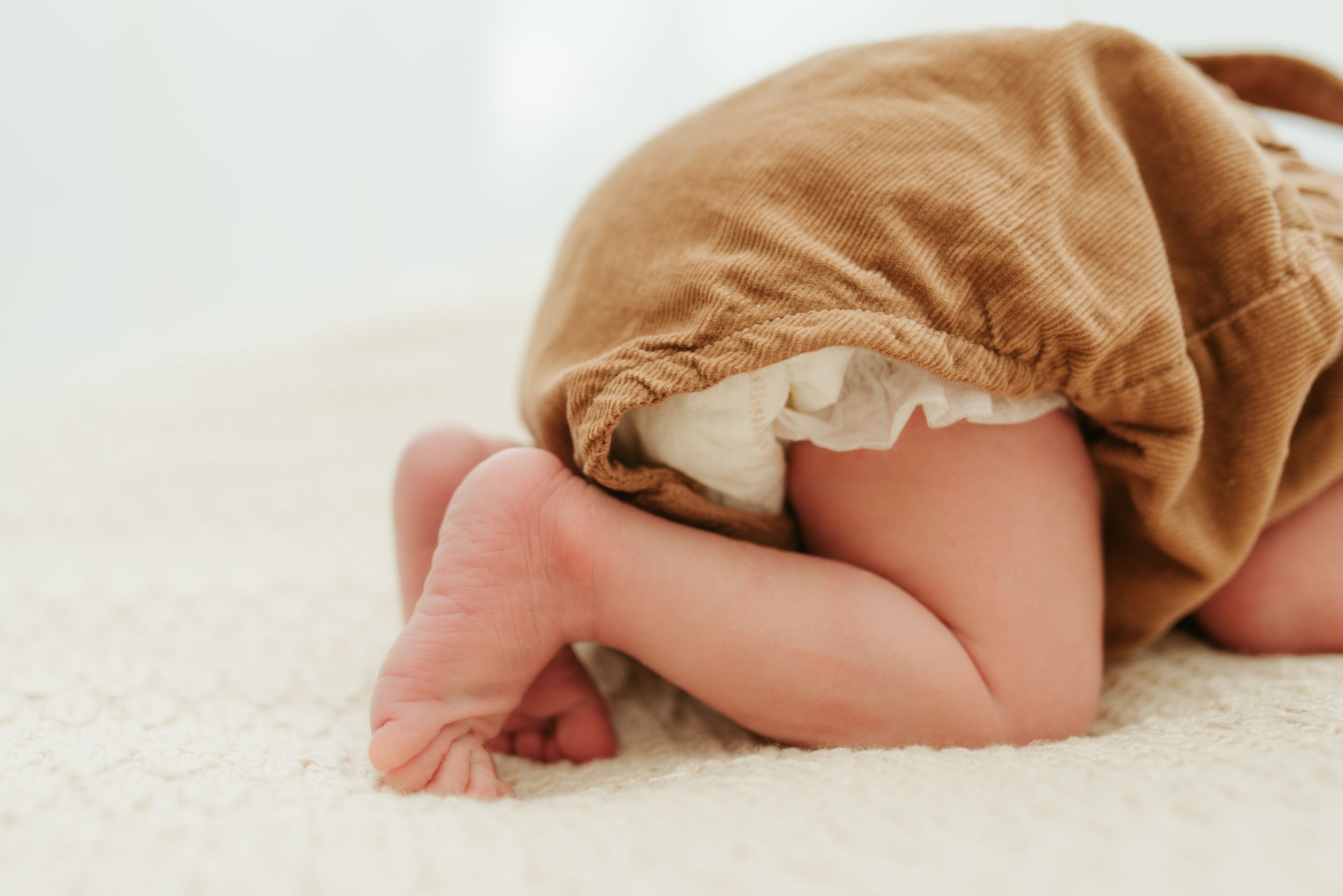 Kleine blote babyvoetjes en billetjes terwijl de bruin pakje draagt. Melissa Stuer Photography Moederschapsfotograaf Moerbeke