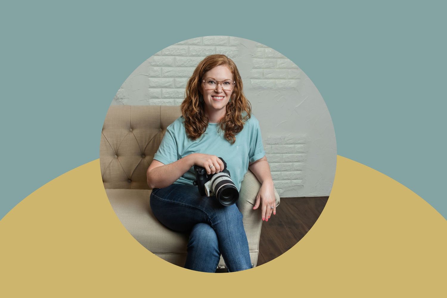 Smiling redhead woman with glasses holding a DSLR camera, sitting on a beige tufted sofa in a modern studio.