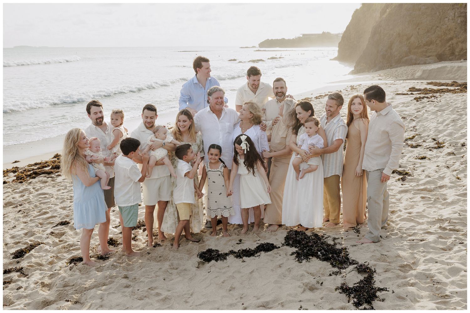 Family portrait on the sandy beach with ocean waves in the background, featuring coordinated neutral and pastel tones.