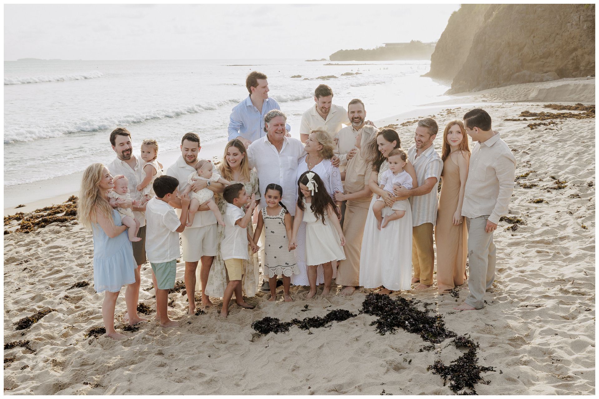 Family portrait on the sandy beach with ocean waves in the background, featuring coordinated neutral and pastel tones.