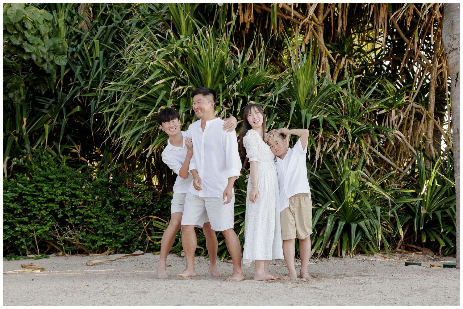Family photo session at The St. Regis Punta Mita with a family laughing together on the sandy beach surrounded by tropical greenery.