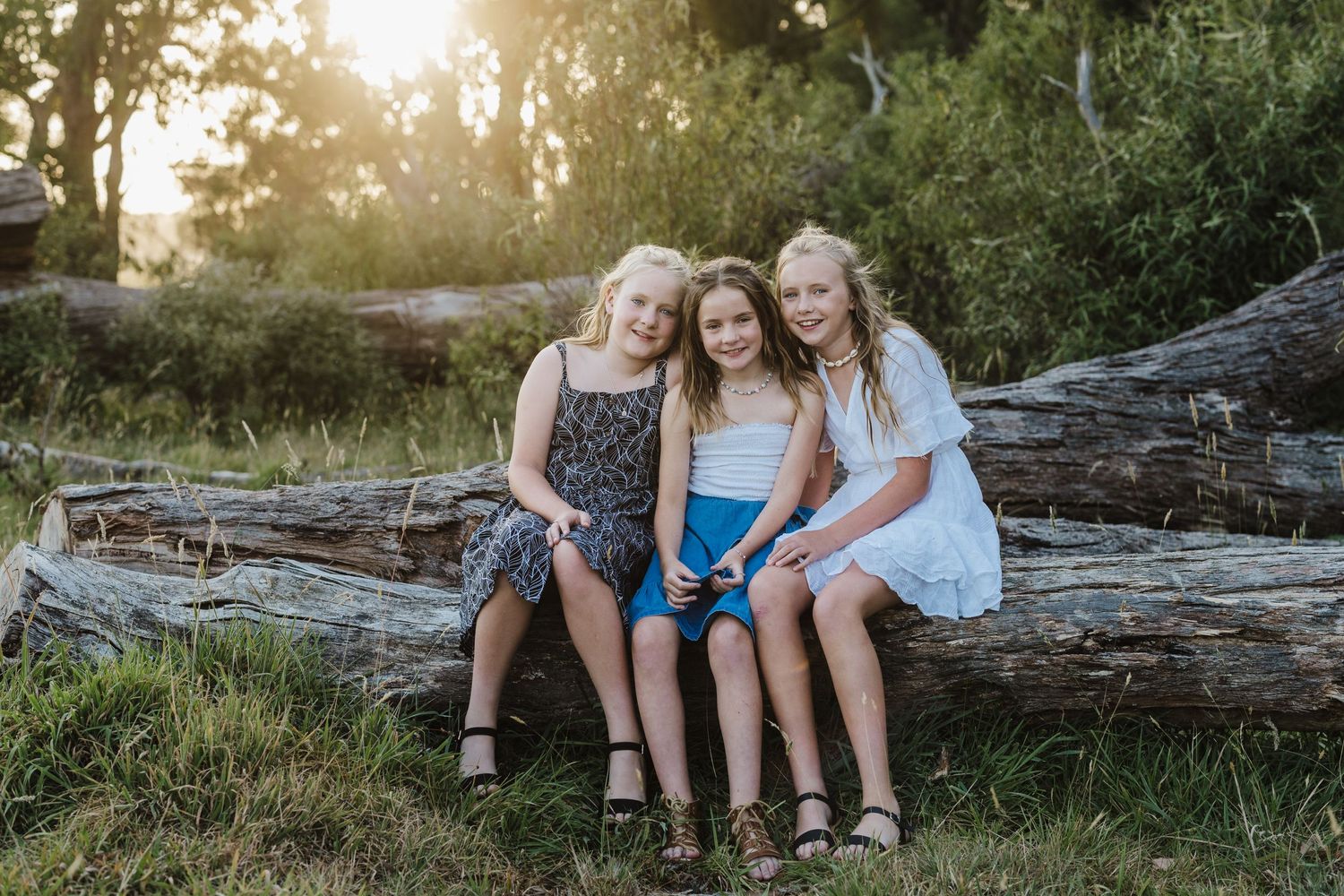 Three friends sitting together on a fallen log at sunset in nature.