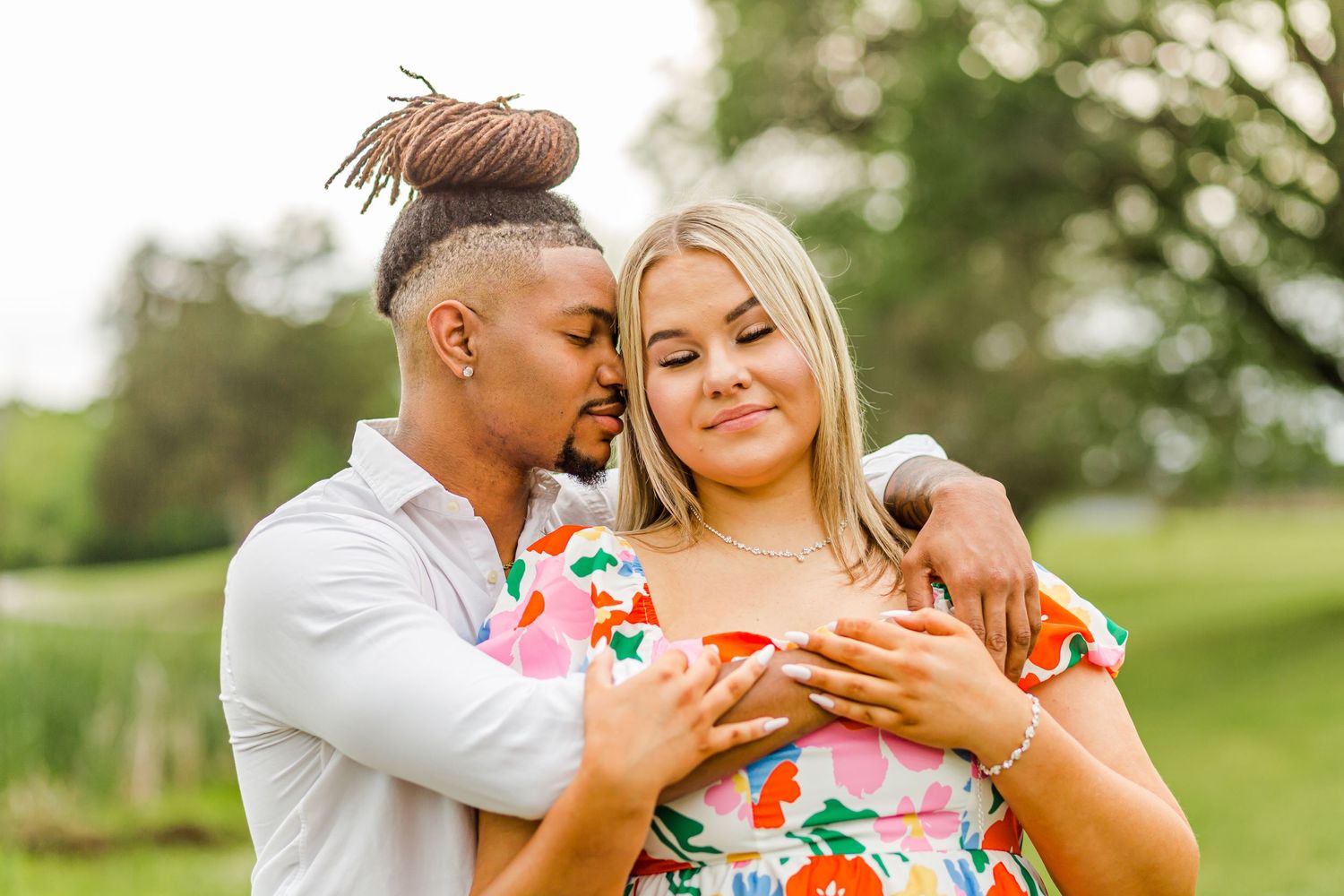 A couple embraces outdoors while looking at something together on a sunny day.