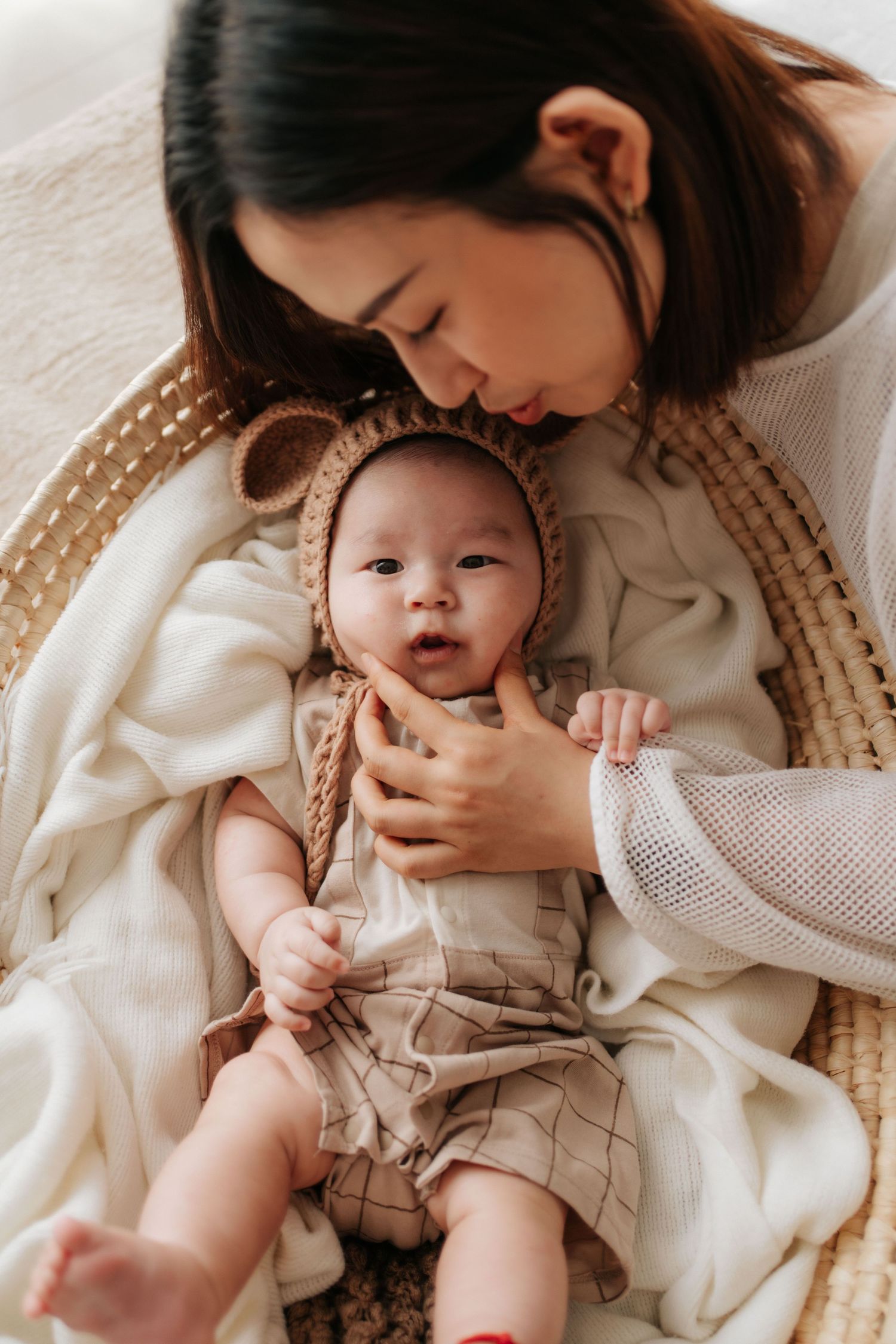 Tender moment with baby in beige clothing resting on white blanket with woven basket in background.