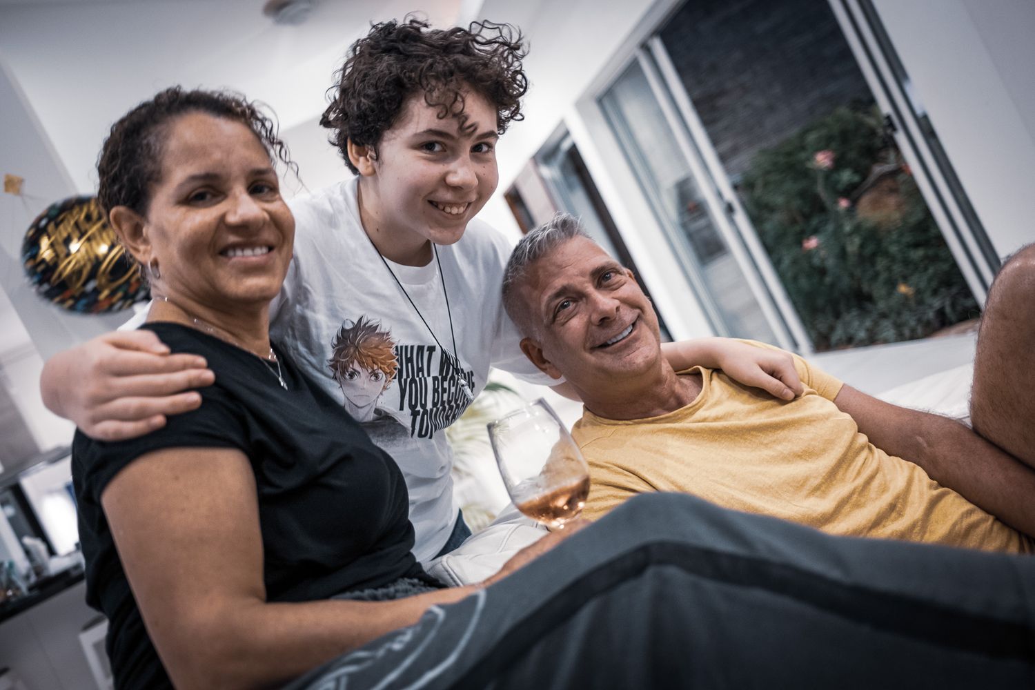 Happy family of three smiling together indoors, with a teenage child between two adults in a warm moment.