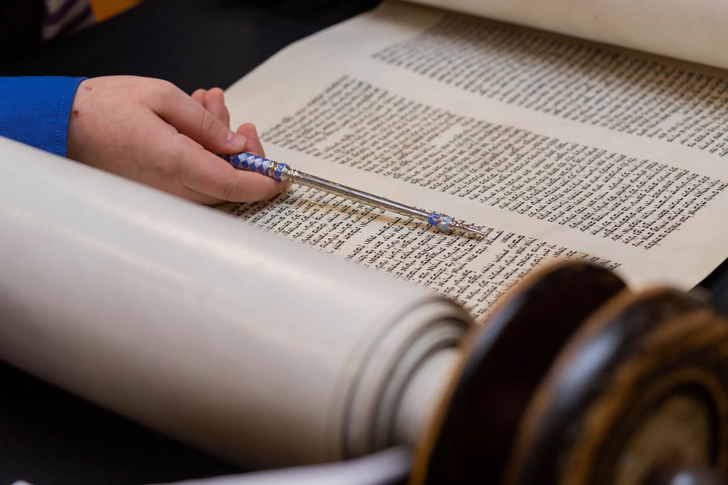 Close-up view of hands following text in an open Torah scroll during a reading.