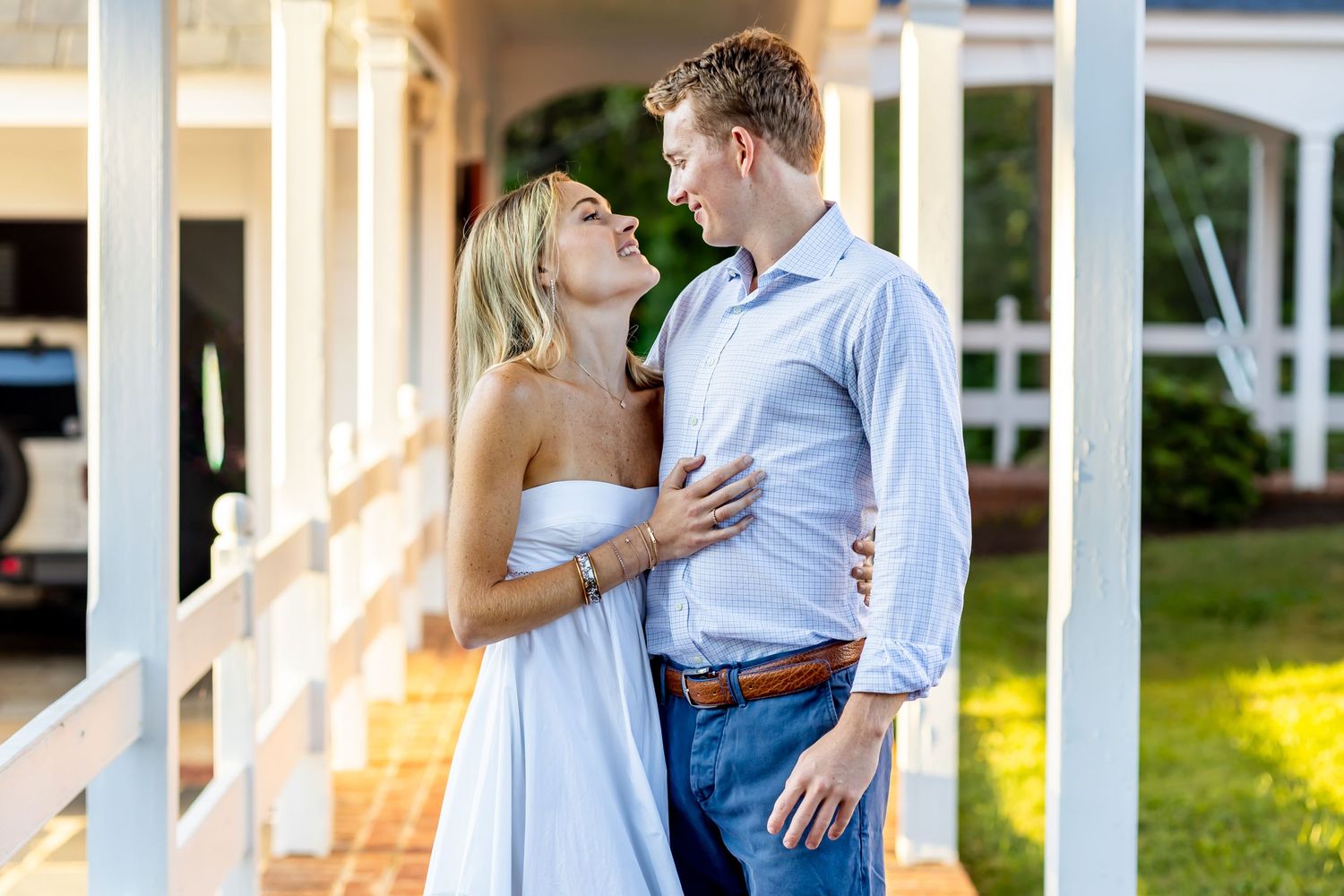 Romantic couple embracing on white porch during golden hour sunset.
