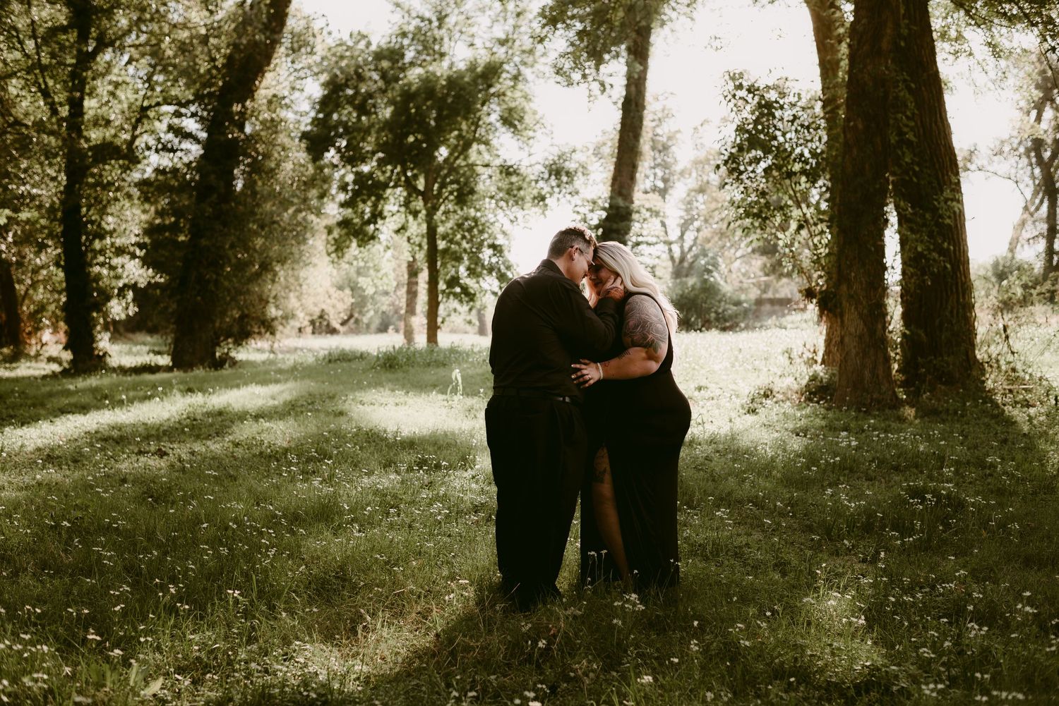 Intimate outdoor couple portrait in a sunlit wooded setting.