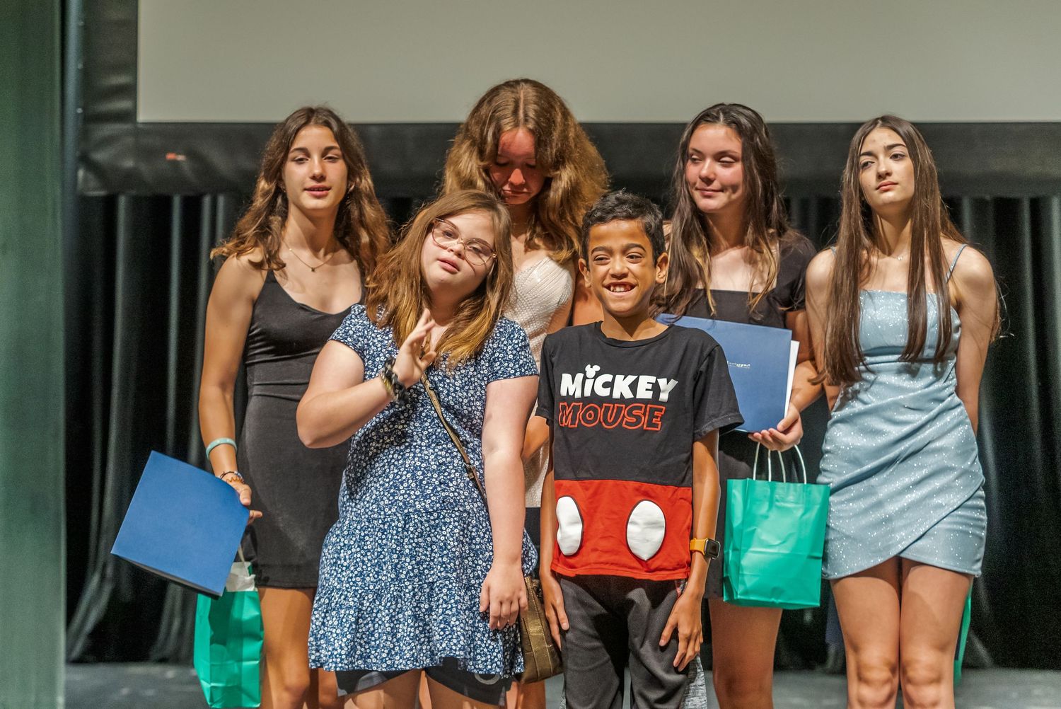 A group poses together on stage during an event with gift bags and signage.