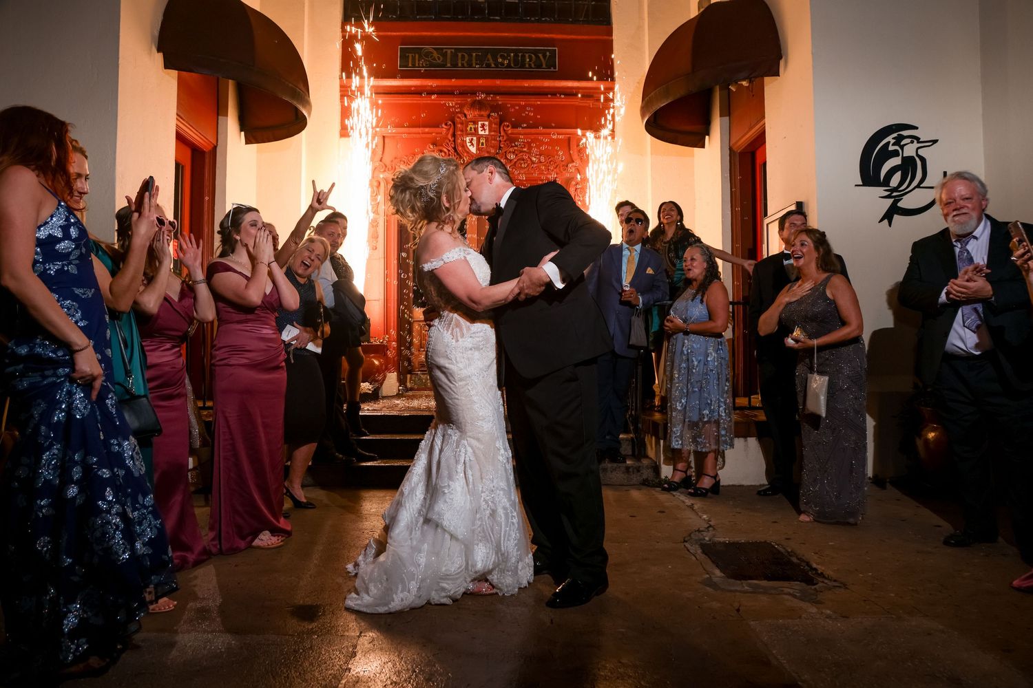 Wedding couple shares dance moment surrounded by guests in dimly lit venue.