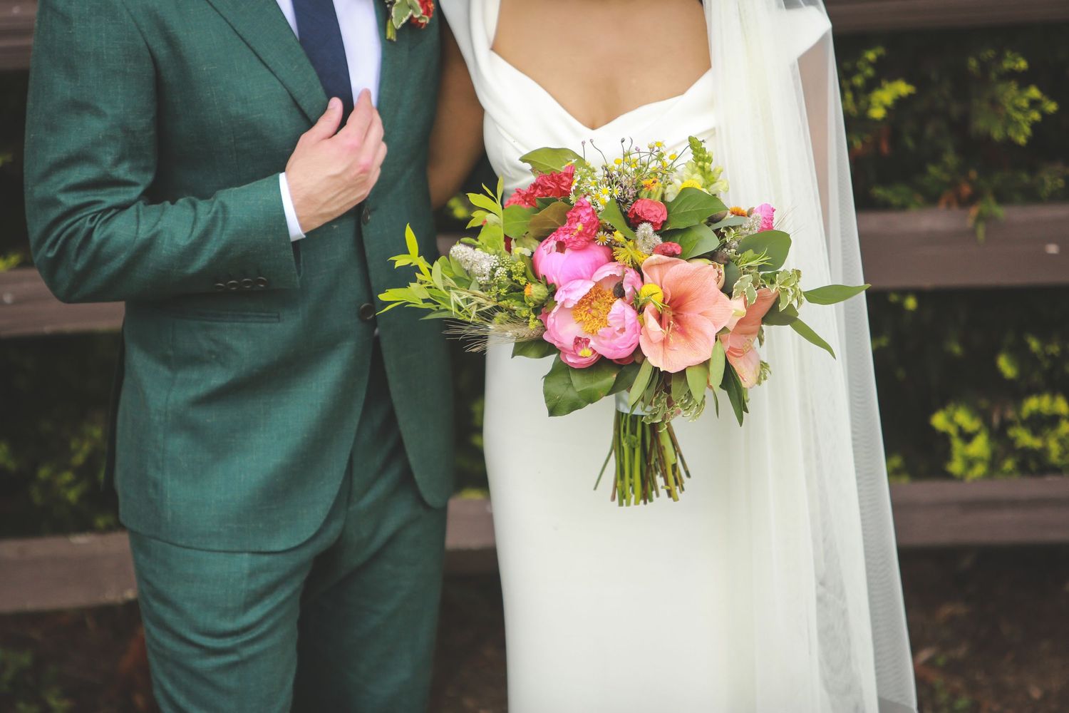 Wedding party members in emerald green attire holding bright pink floral bouquets.