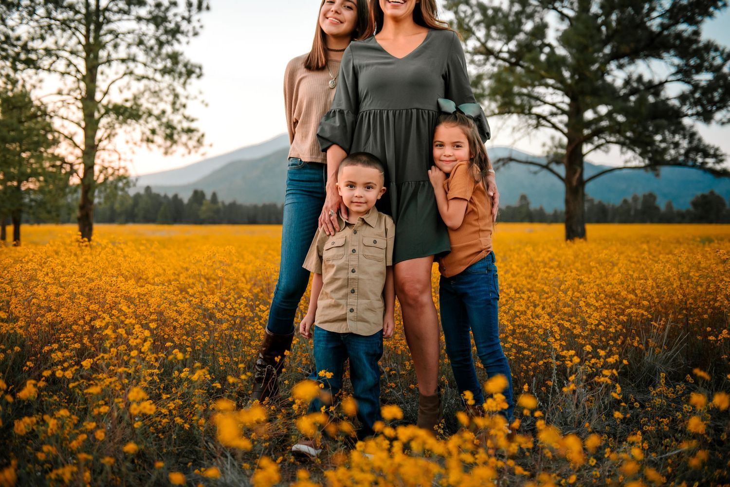 Family standing together in a vibrant field of yellow wildflowers at sunset.