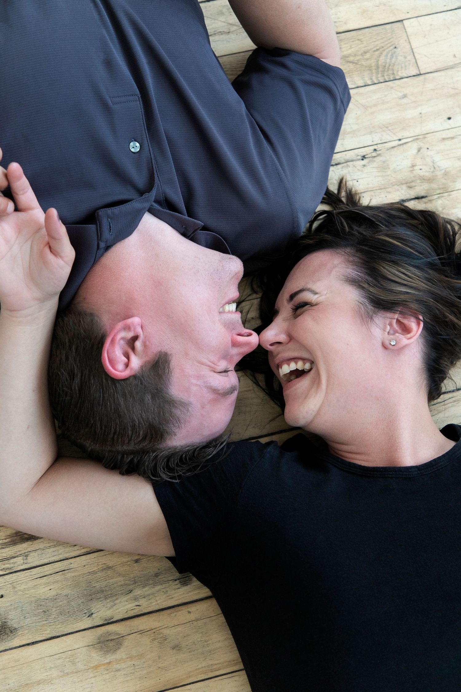 a couple lying on the floor with their heads together and their bodies facing the opposite directions leaning in and smiling