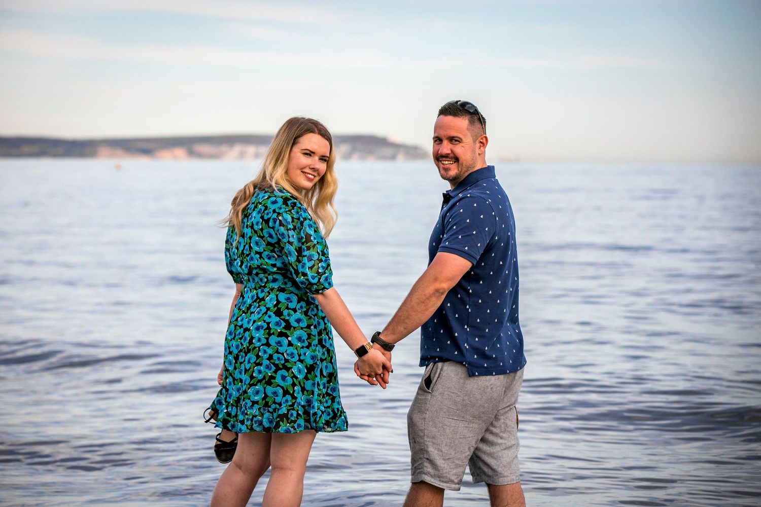 A couple holds hands while walking along the beach in coordinated blue outfits.