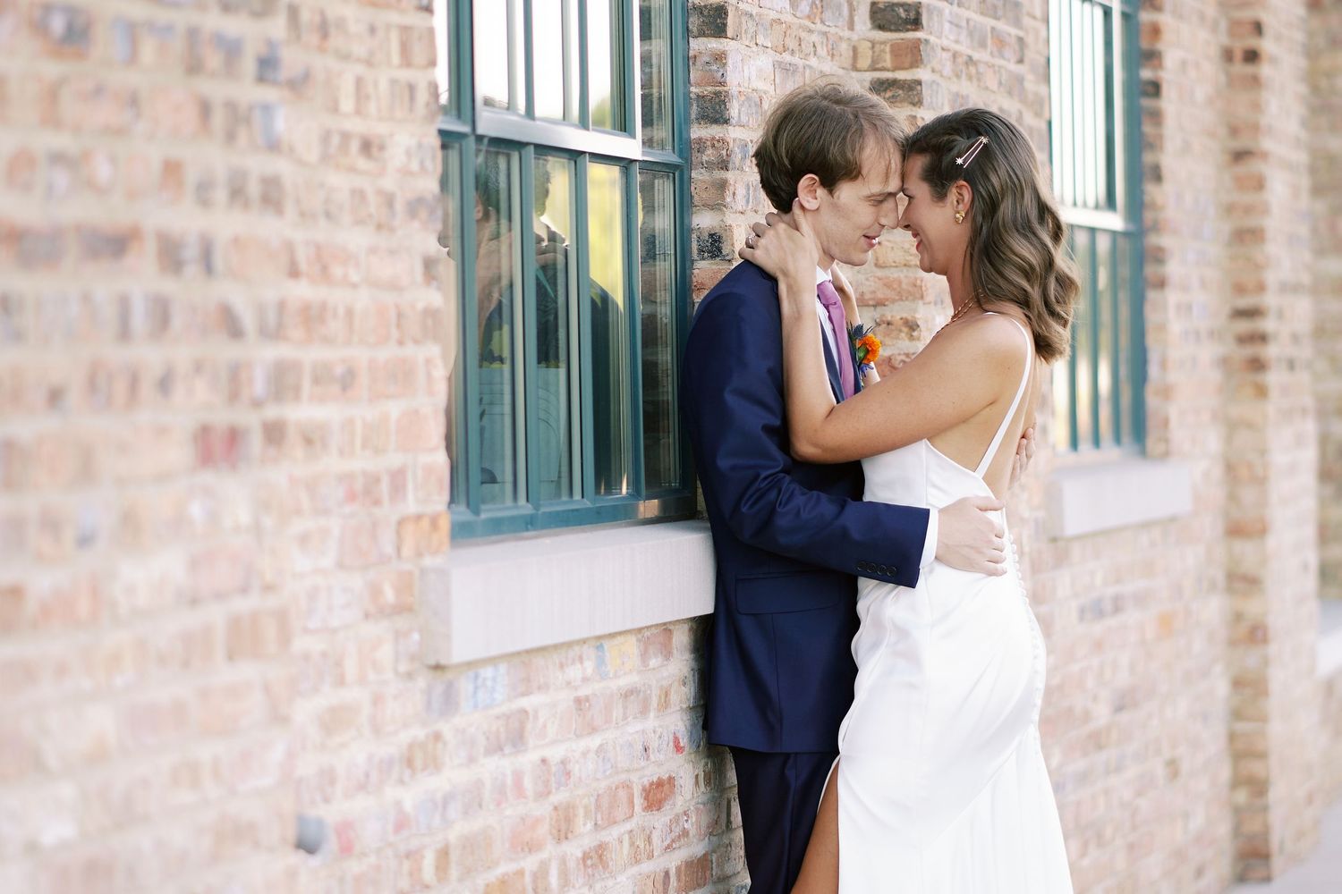 A romantic moment against a rustic brick wall with green window frames.