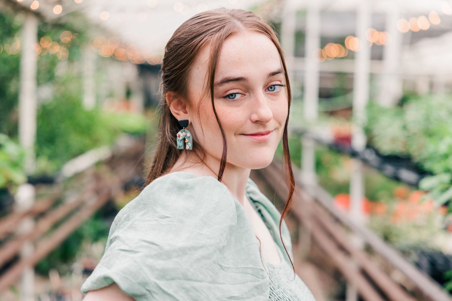 Portrait in garden setting wearing sage green dress and vintage earrings.